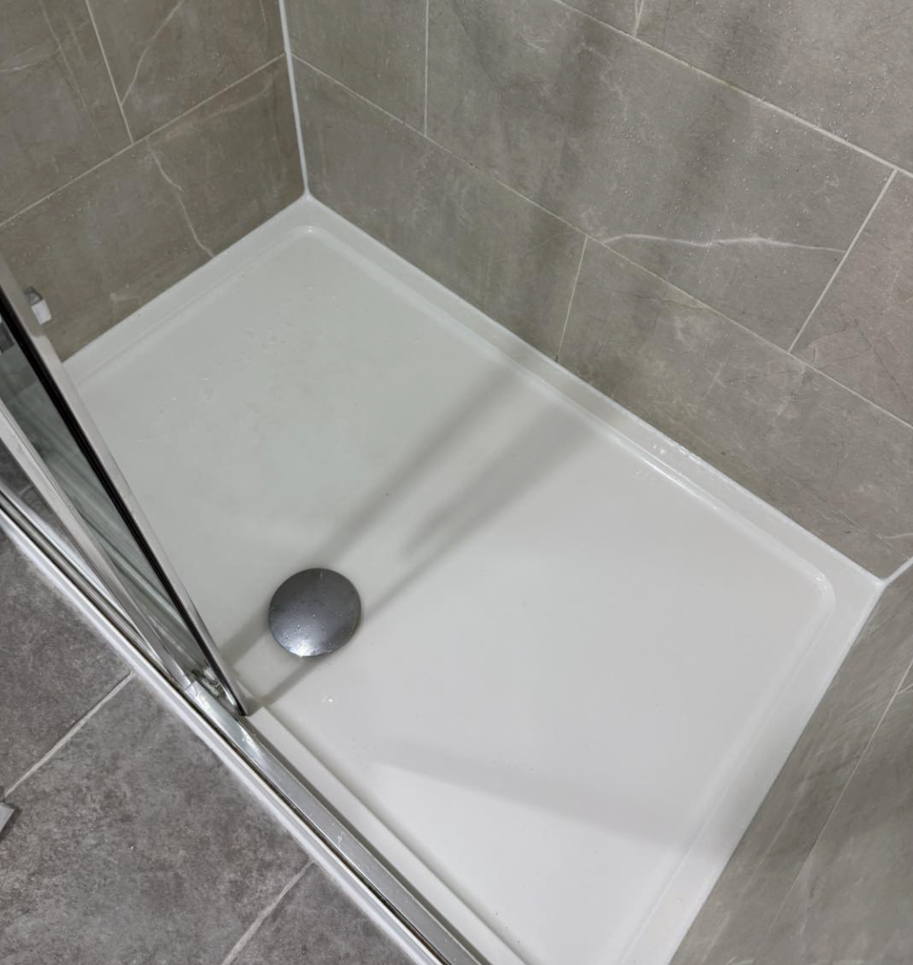 Empty shower stall with a chrome drain and a glass door, tiled with large gray tiles.