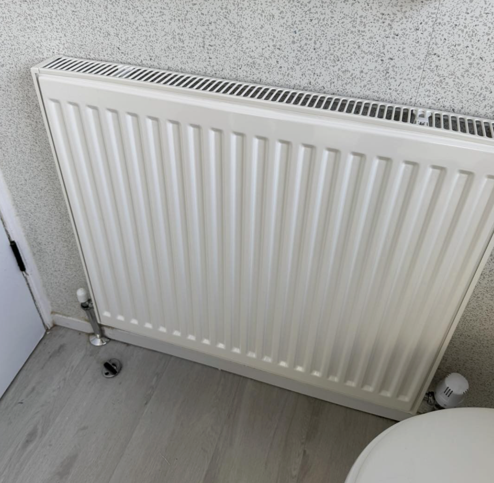 A white radiator radiator mounted on a speckled wall next to a door and a toilet in a bathroom.