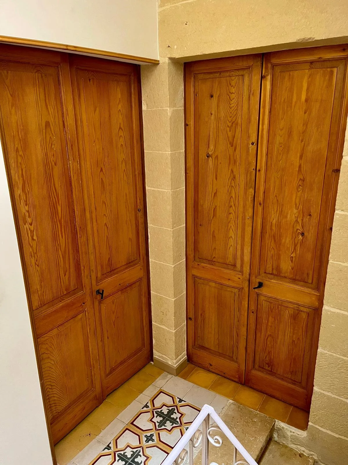Wooden cabinet doors at a staircase corner in an indoor space with beige brick walls and patterned floor tiles.