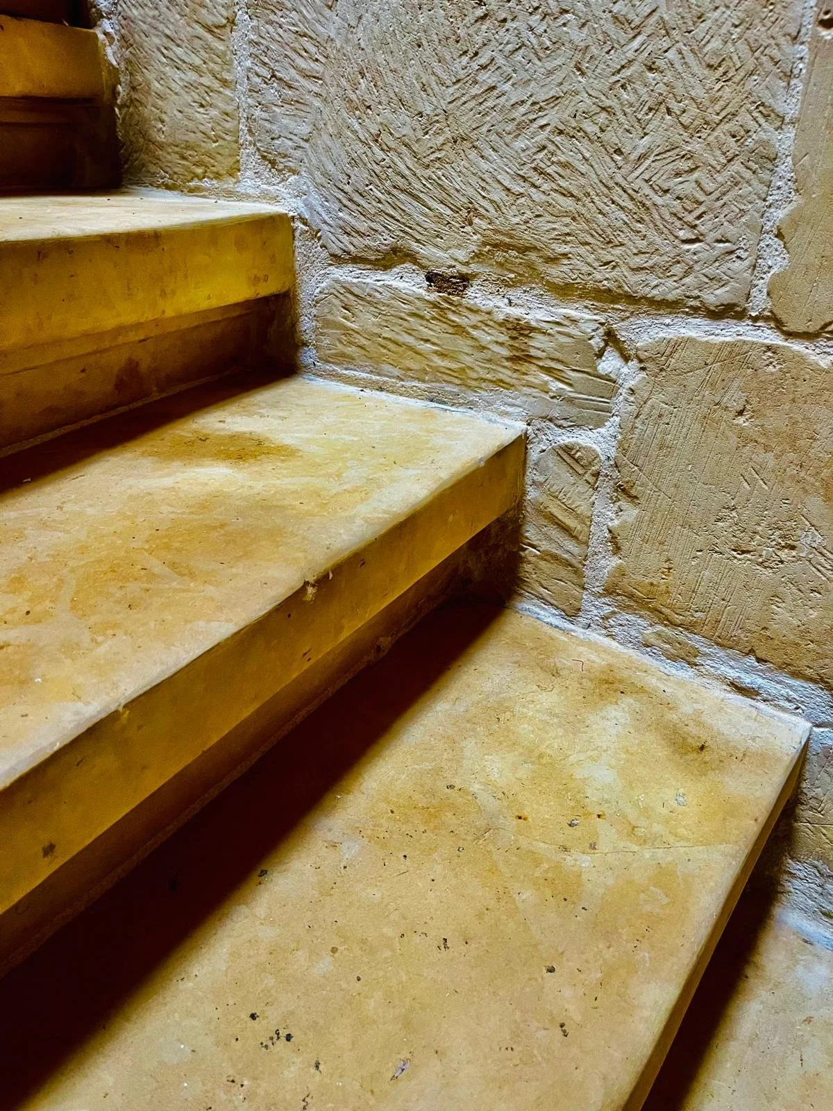 Close-up of stone stairs with yellowish marble steps and textured beige stone walls.
