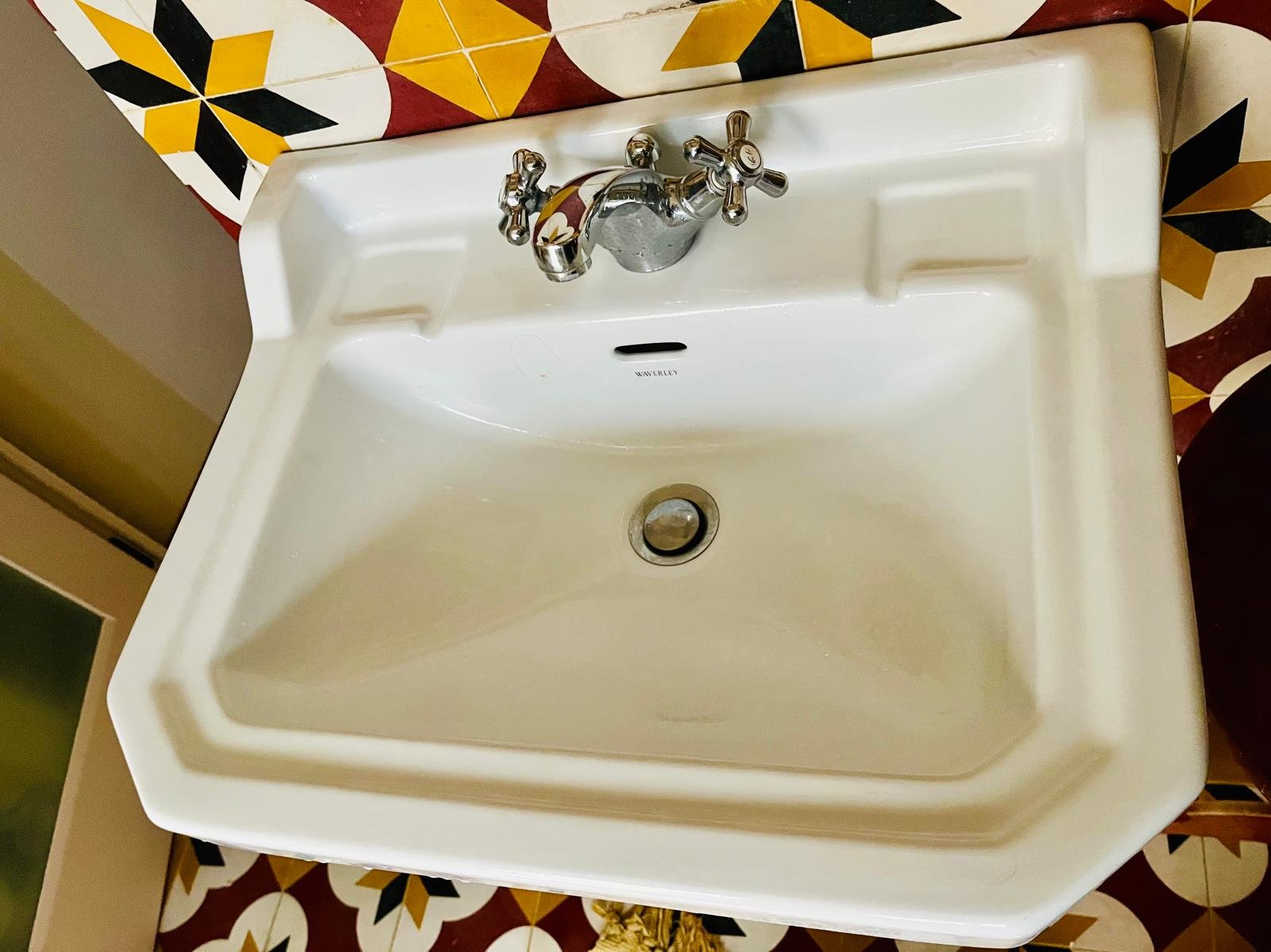 White vintage sink with chrome faucet, mounted on a wall with a patterned tile background.