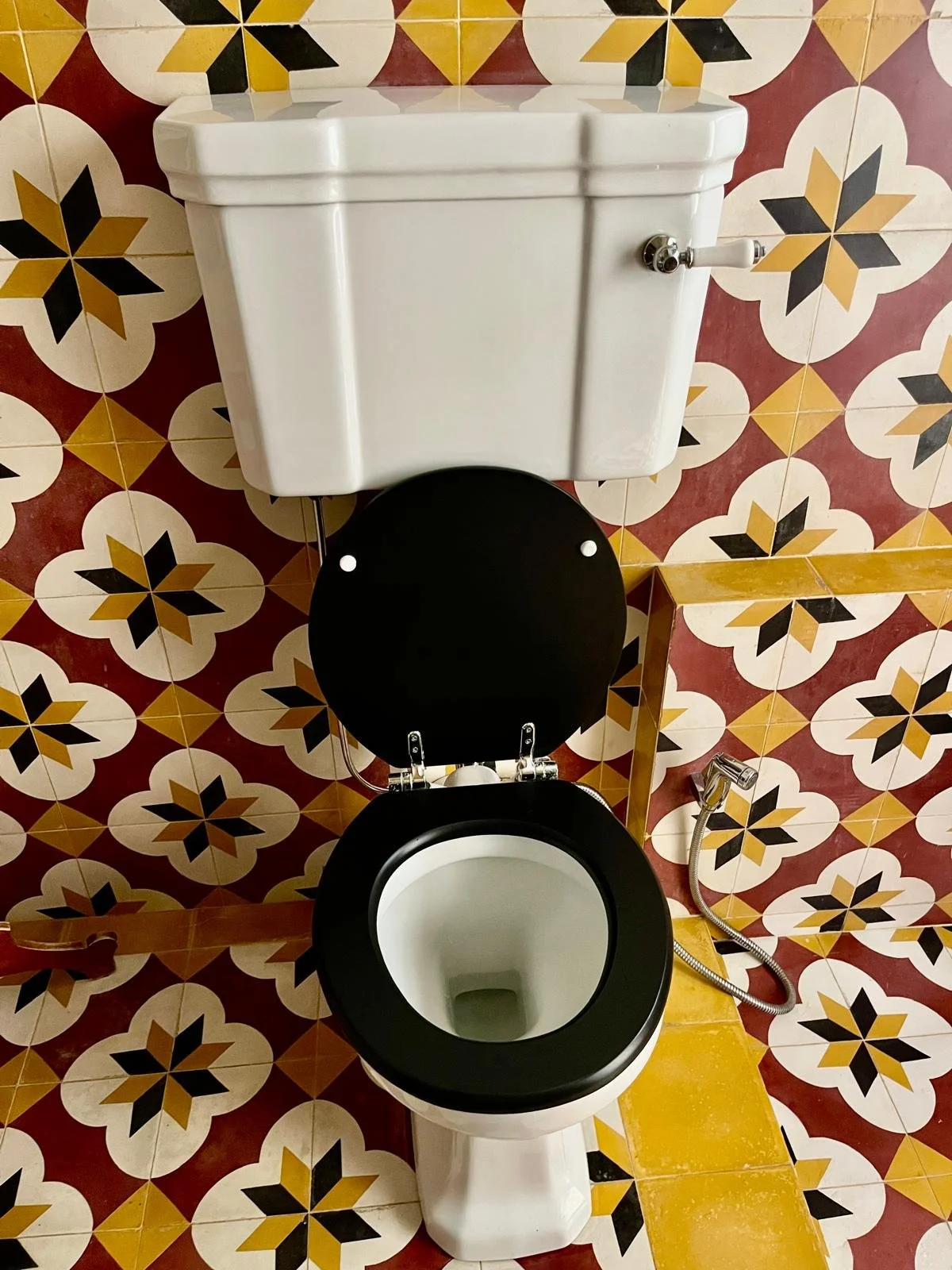 A toilet with the lid open, set against a patterned tile wall and floor.