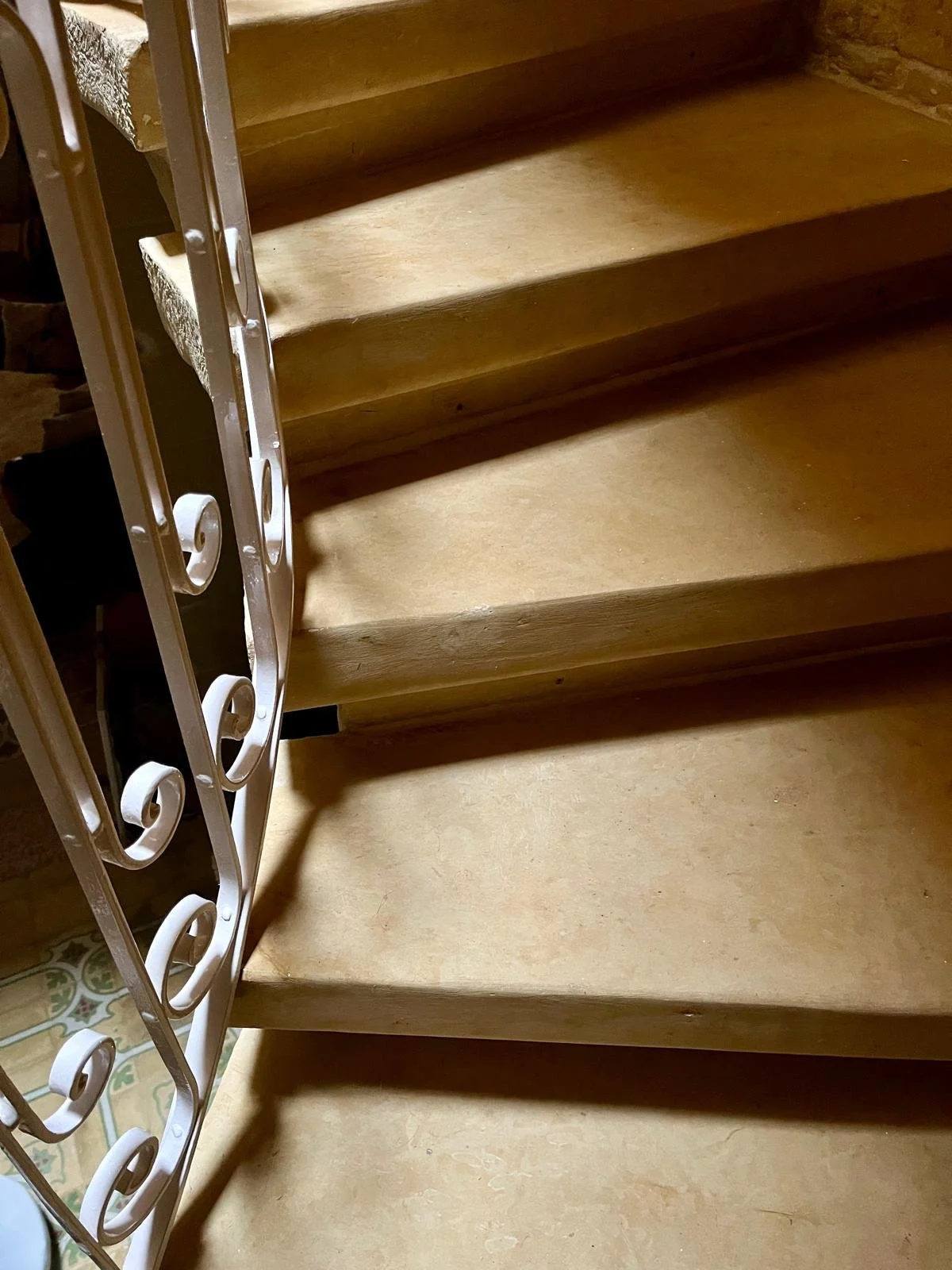A close-up view of wooden stairs with a decorative metal railing on the left side.