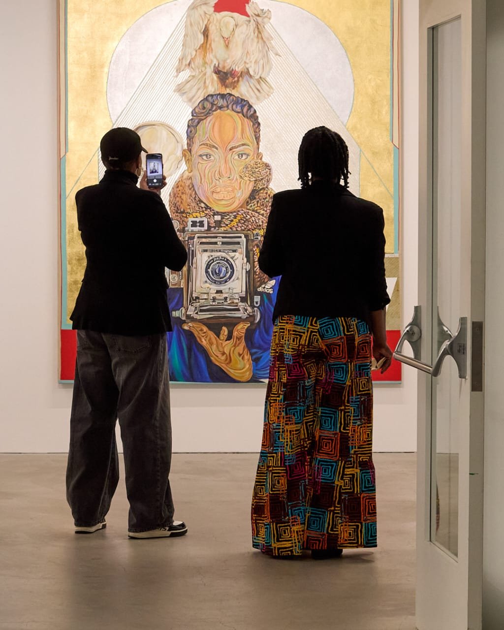 Two people standing in front of a colorful large painting of a portrait by acclaimed South African artist, Ayanda Mabulu in an African contemporary art gallery, Art of Contemporary Africa (AOCA)