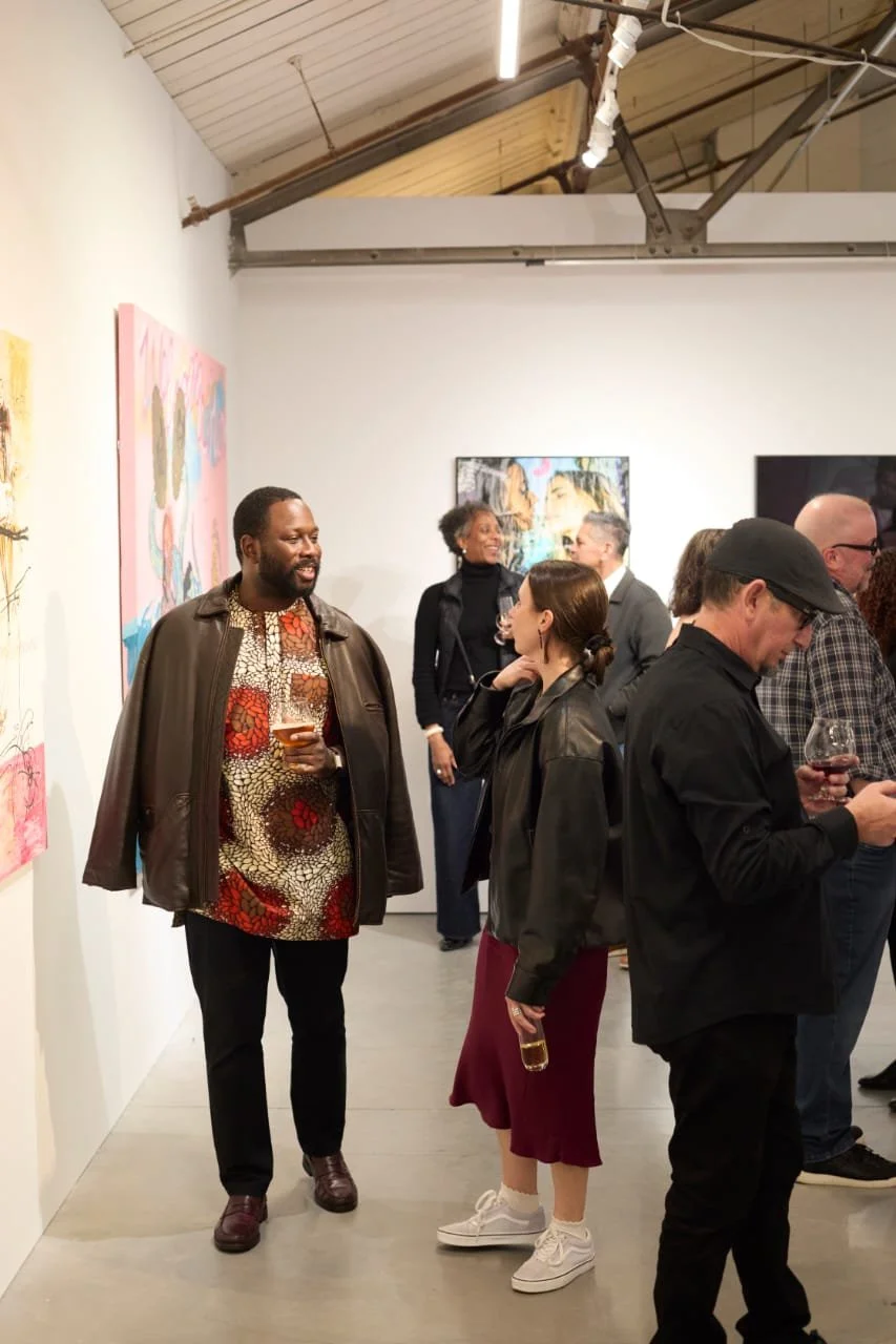 People socializing at an art gallery exhibition, viewing and discussing colorful African artwork on the walls at Minnesota Street Project for Art of Contemporary Africa inaugural opening and exhibition