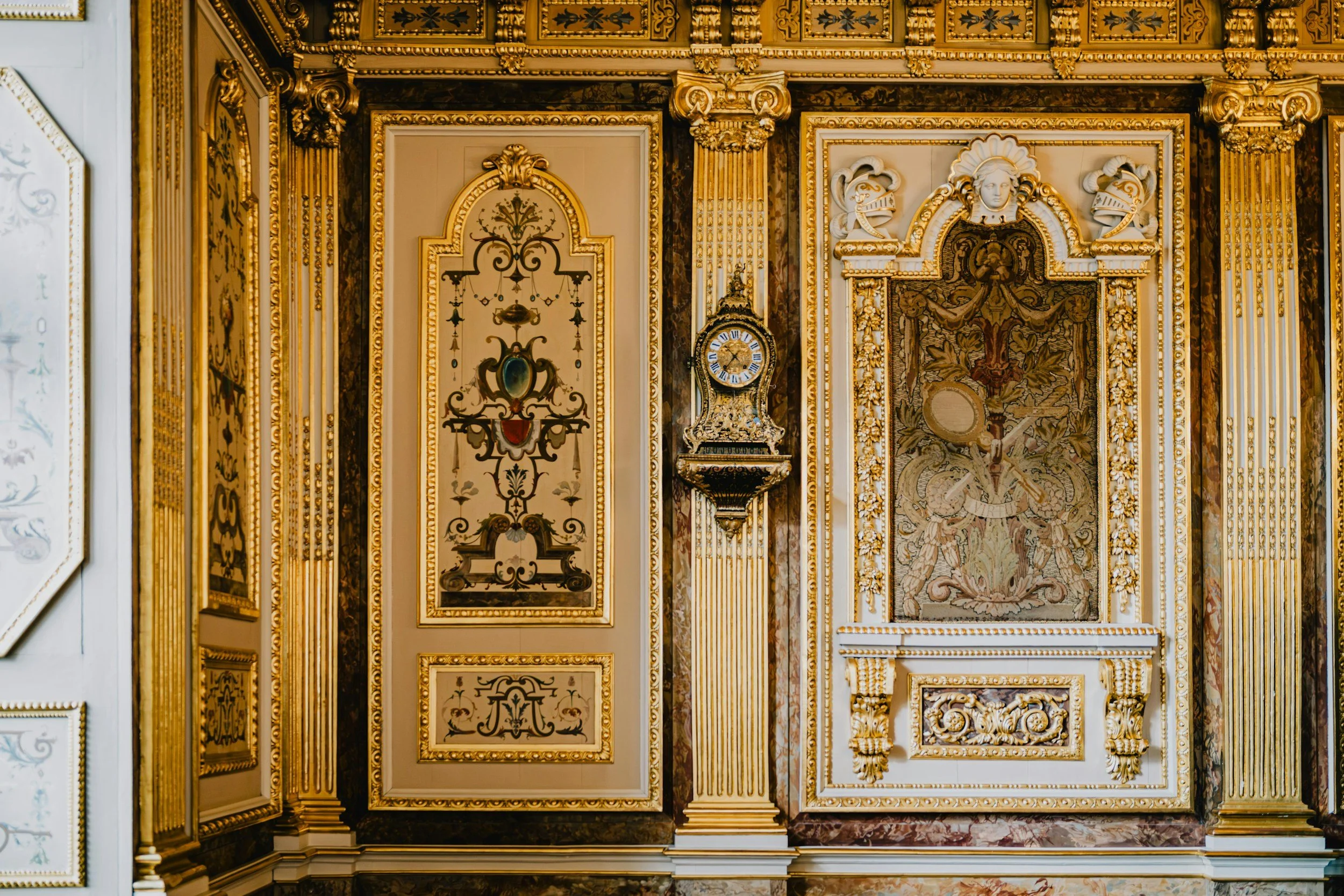 An ornate wall with gold accents, decorative panels, a clock, and intricate artwork in a historic building.