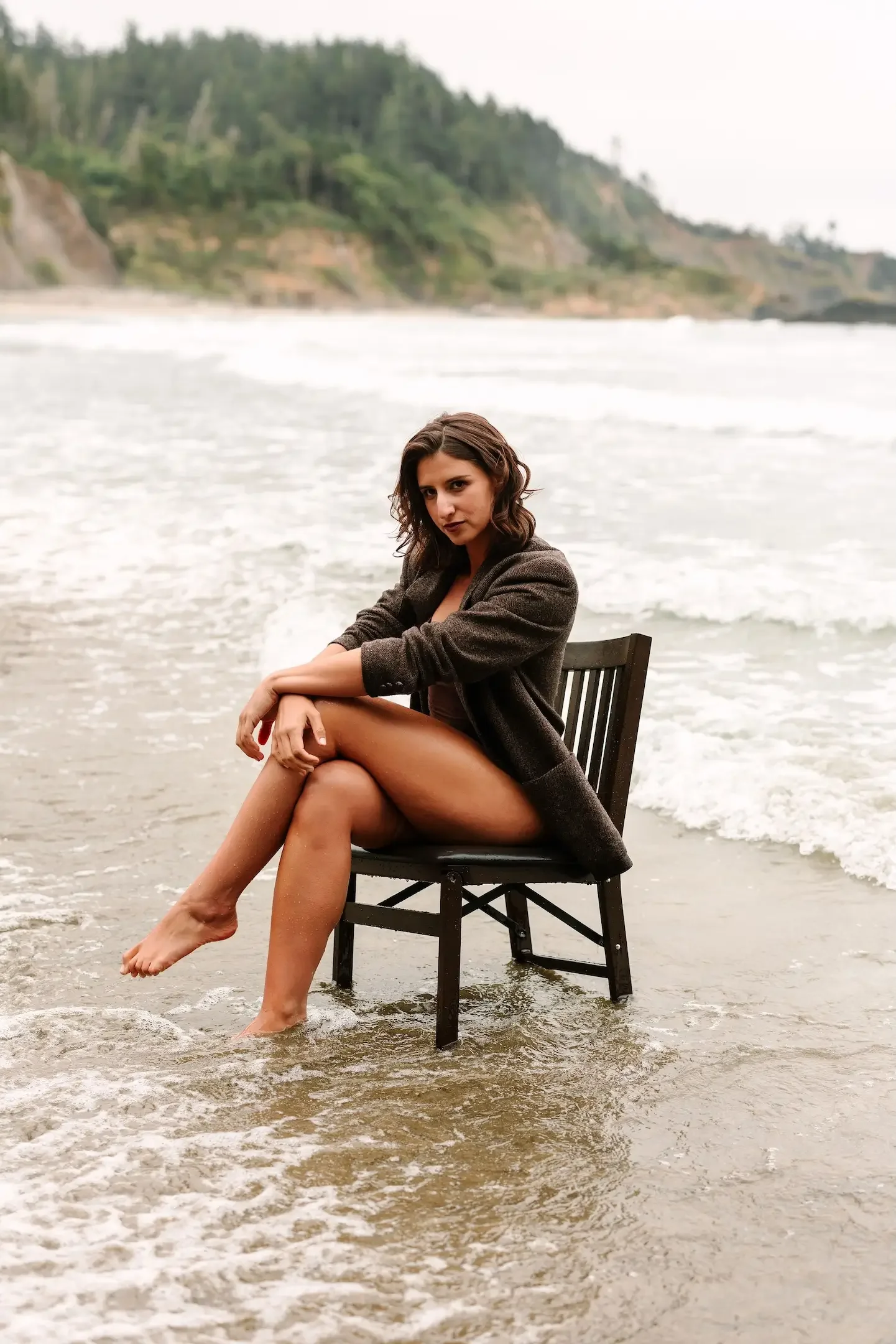 Leadership coach, Hélène Caniac, sitting on a chair in the ocean waves at the beach with a mountain and trees in the background.