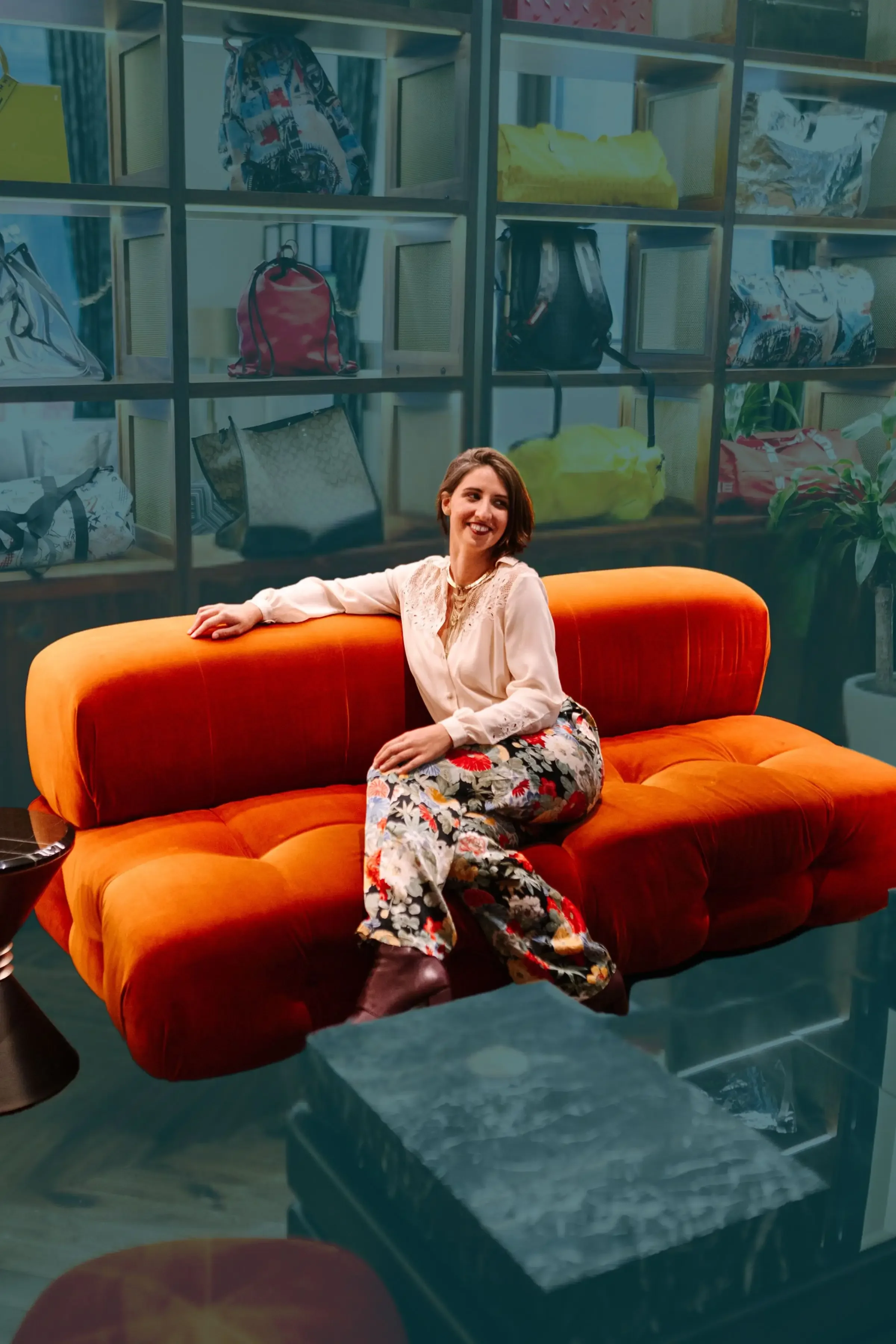 Hélène sitting on an orange sofa in a modern, cozy room with a bookshelf filled with books behind her.