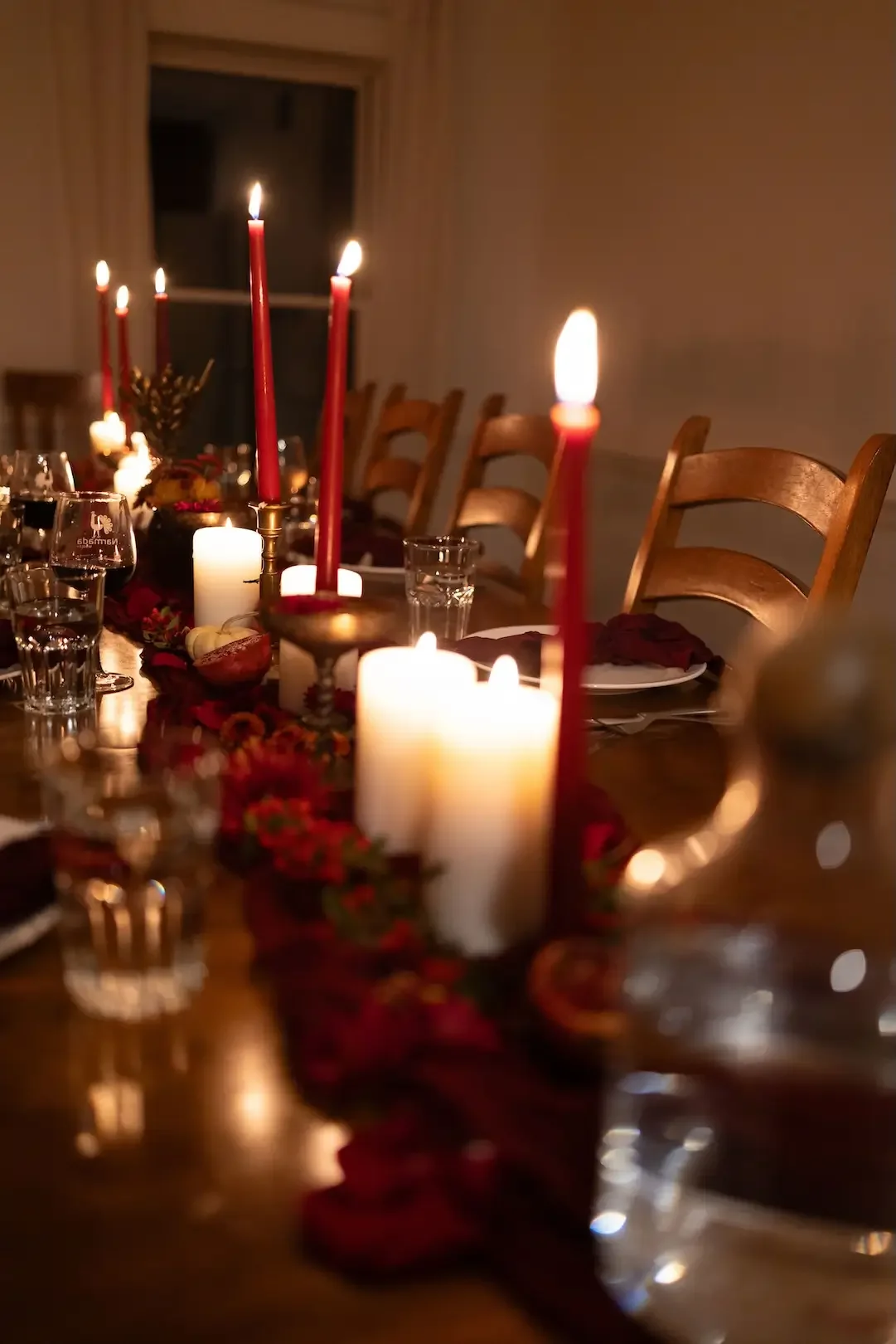 A dimly lit dining table decorated with red candles, white candles, and red wreaths, set for a holiday celebration.