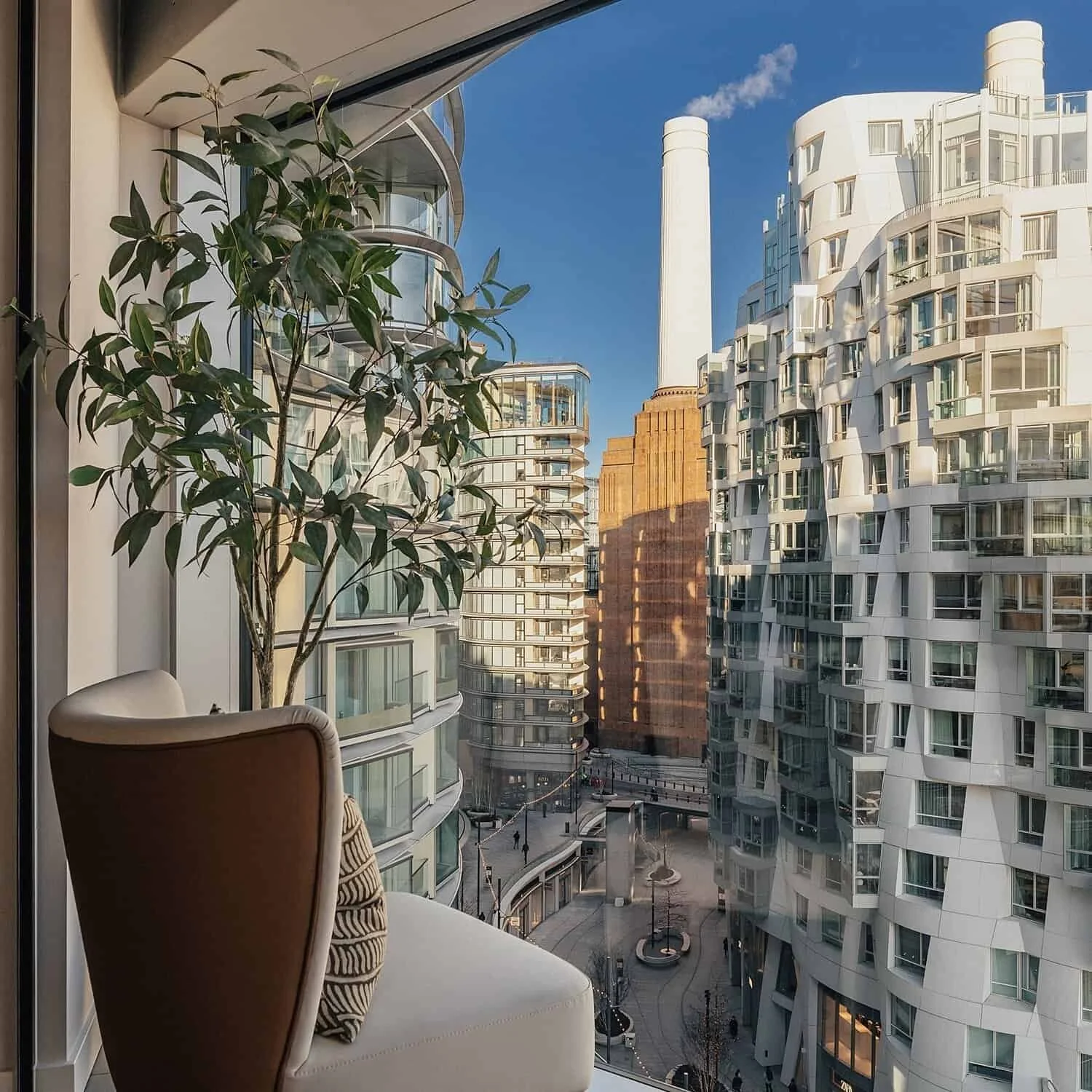 Balcony view of modern high-rise apartment buildings with curved glass facade, greenery, and a clear blue sky.