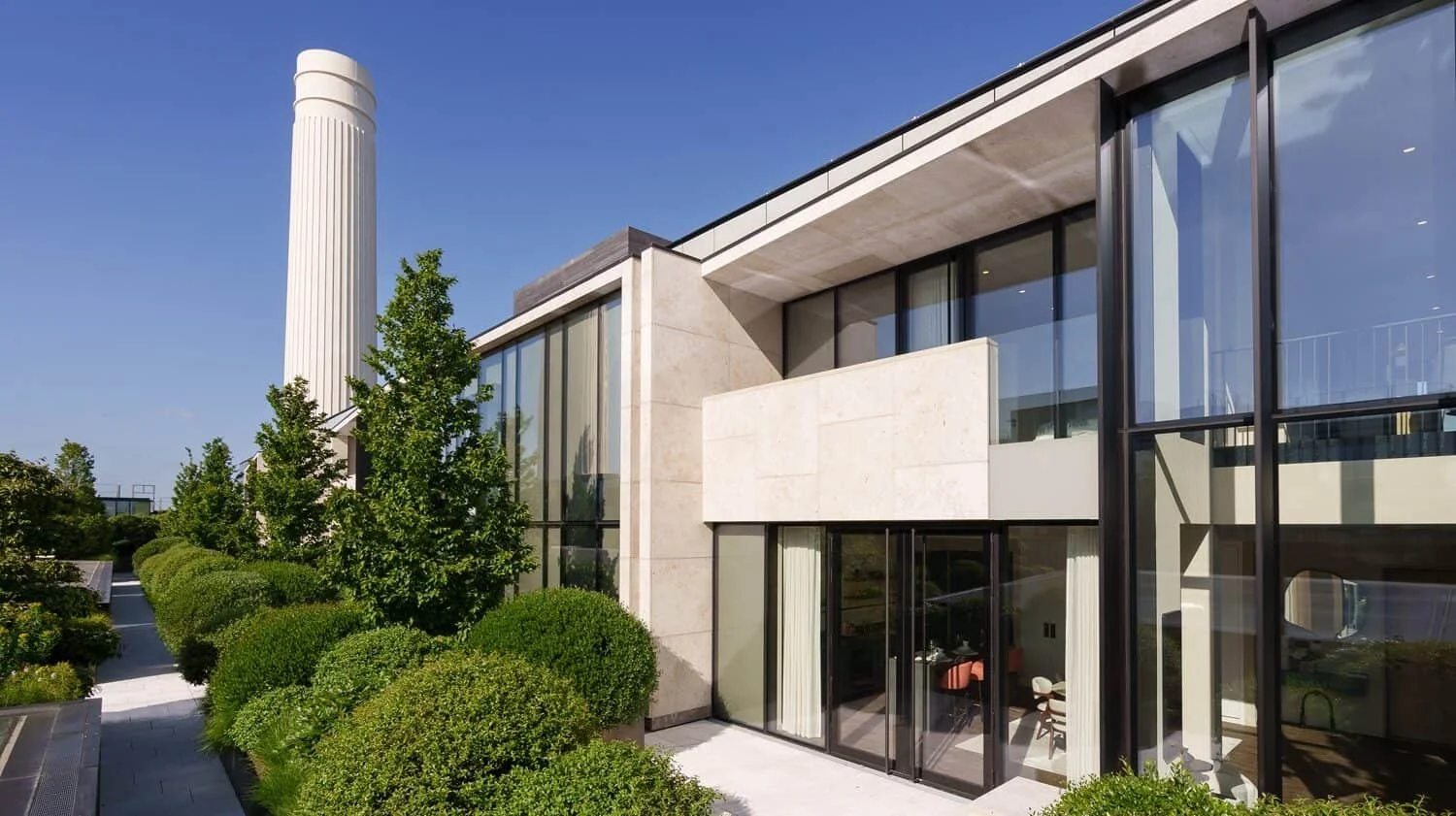 Modern residential building with large glass windows and a landscaped garden with shrubs and trees.