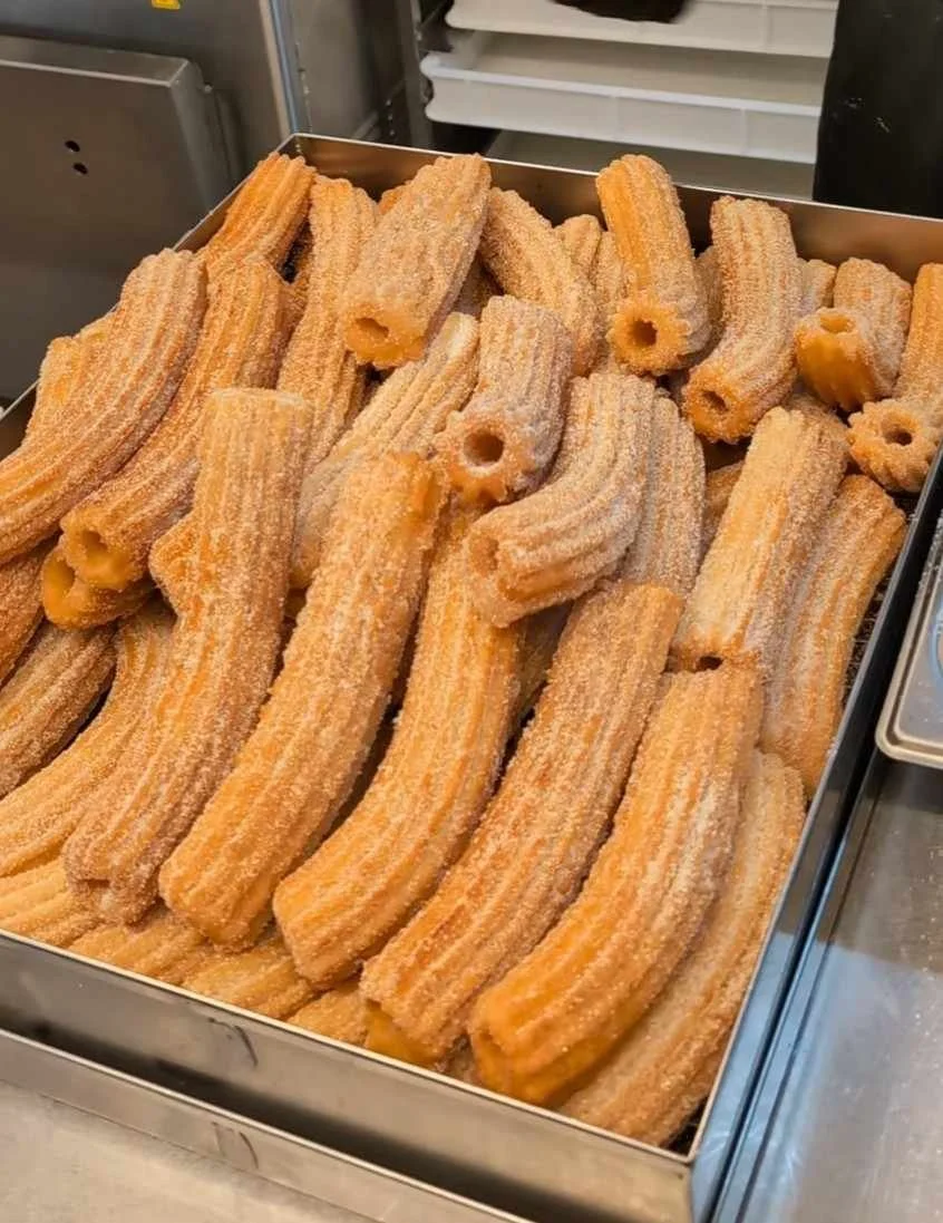 A tray of raw churros coated with sugar and cinnamon, ready for frying.