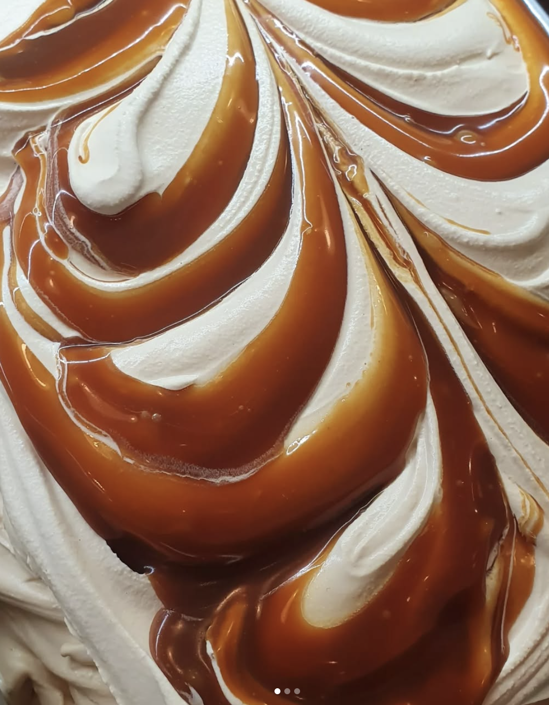 Close-up view of swirled vanilla ice cream with caramel sauce drizzle.