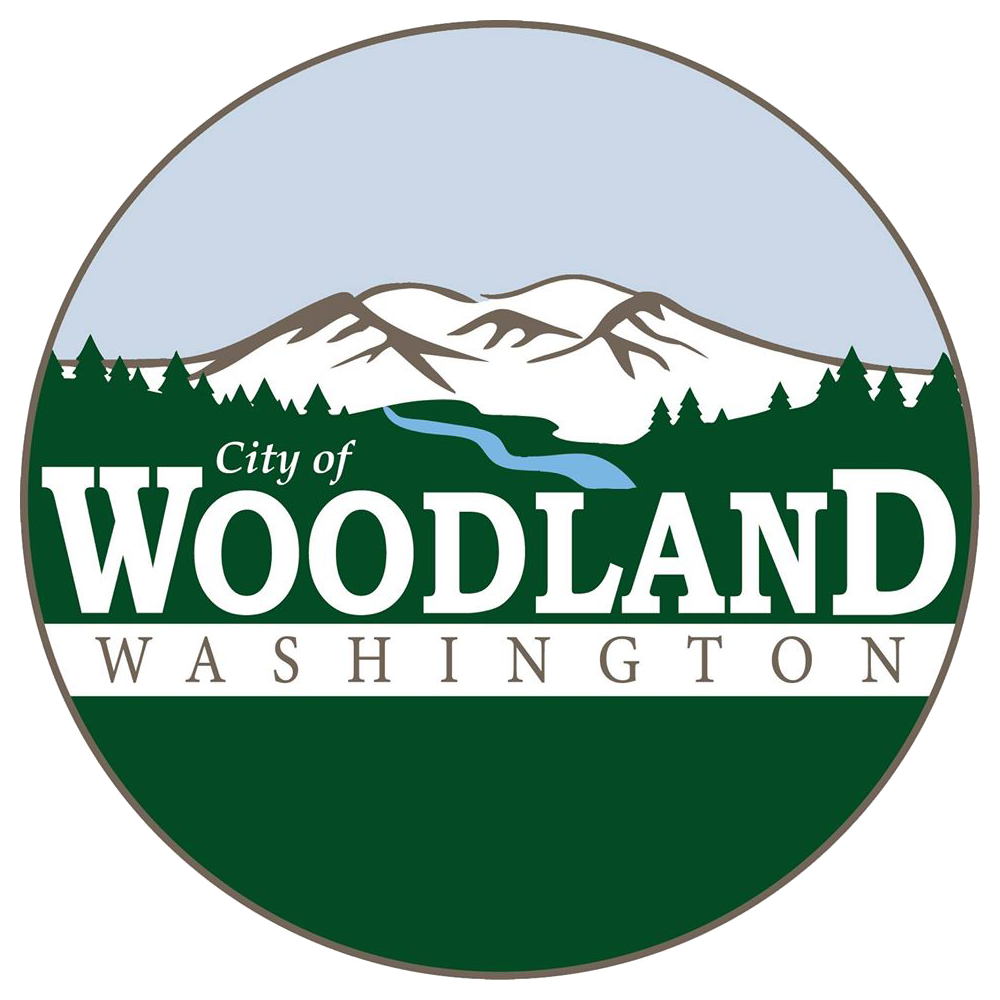 A circular logo with mountains, trees, and a river, with the text "City of Woodland Washington".