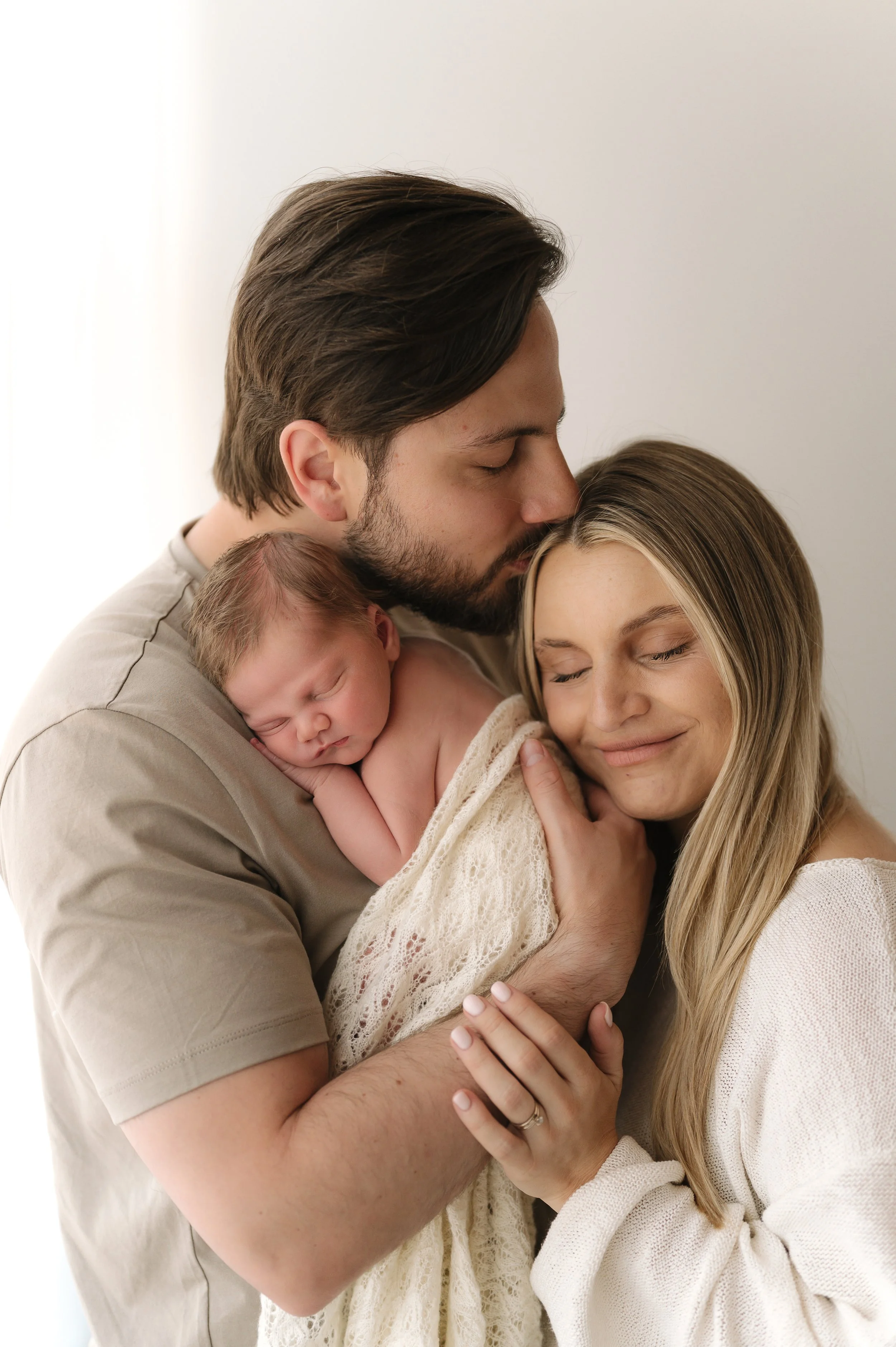 A couple holding their sleeping newborn baby close to their faces with affection.