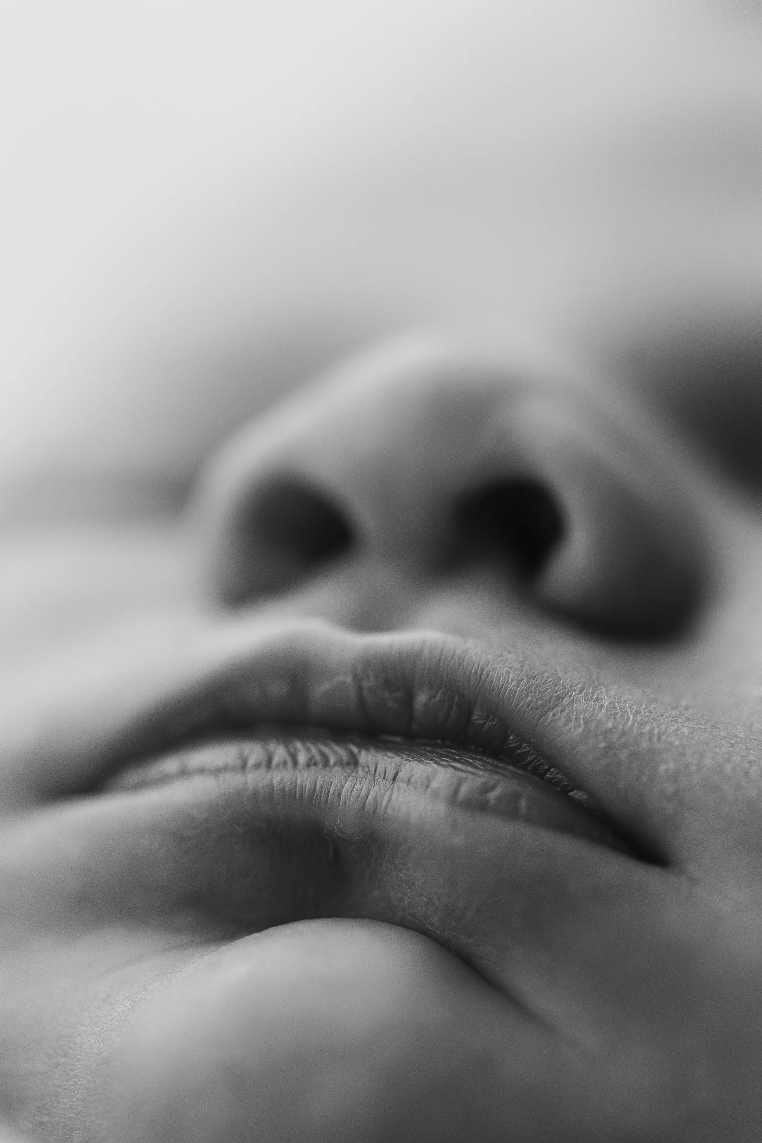 Close-up black and white photograph of a person's nose and lips, with the face upside down.