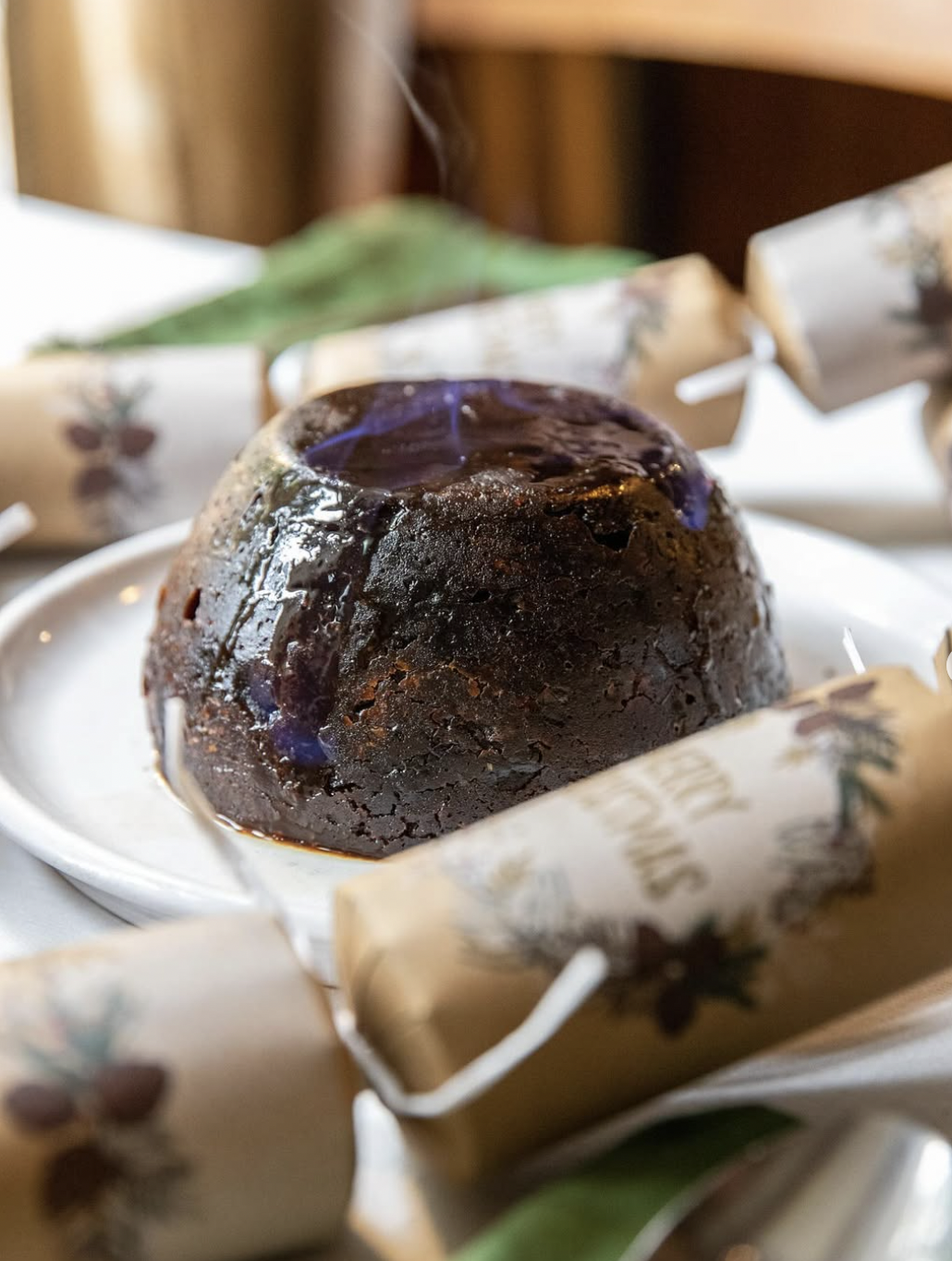 A chocolate lava cake with a shiny, melted top on a white plate, wrapped with holiday-themed paper.