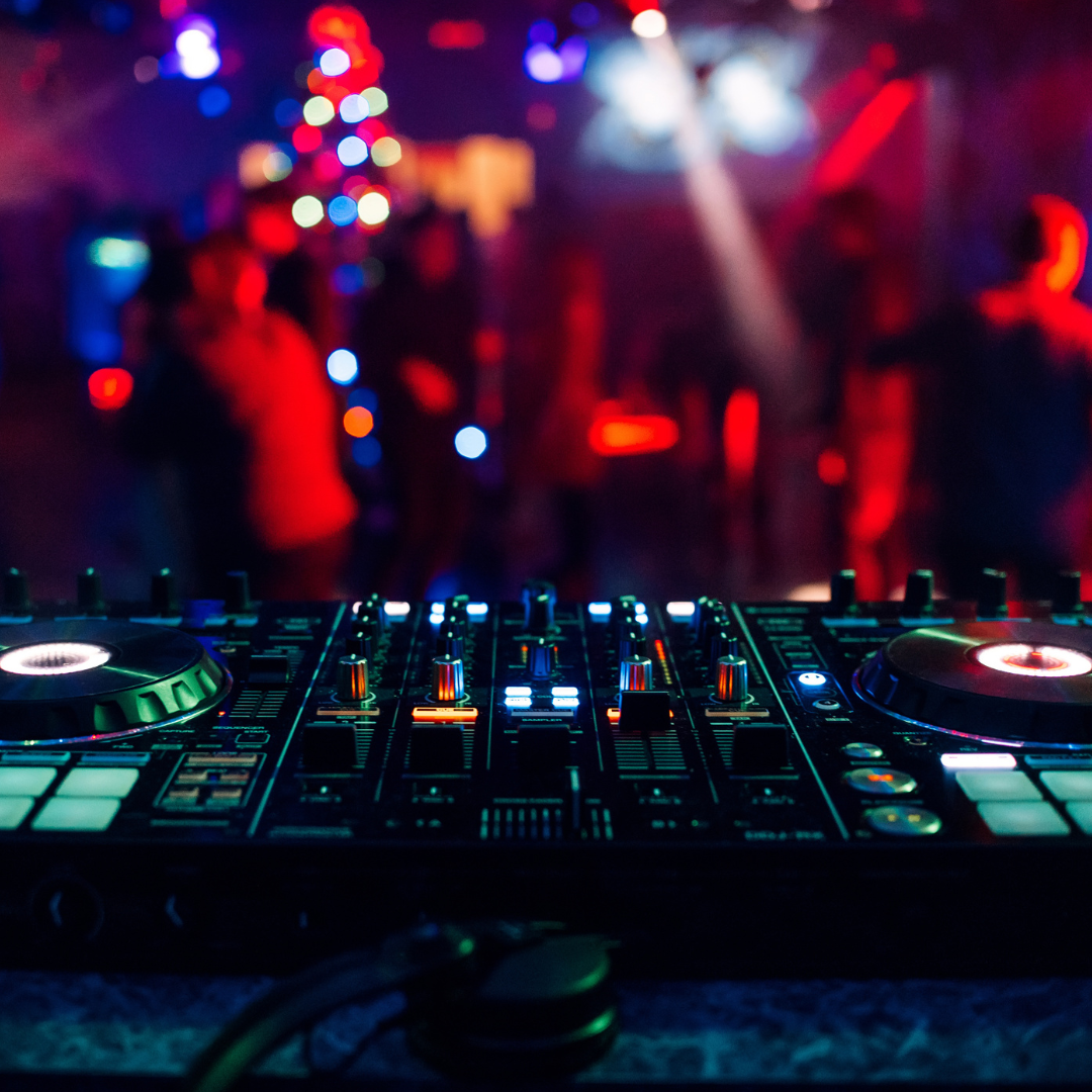 DJ controller with glowing colorful lights in a blurred nightclub setting.