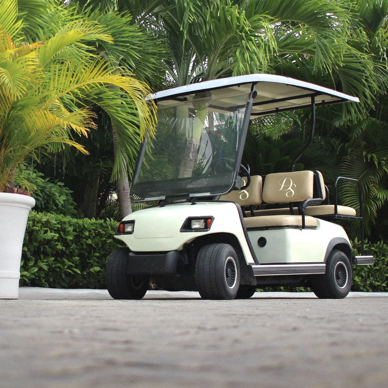 A white luxury golf cart parked in a tropical garden setting with palm trees.