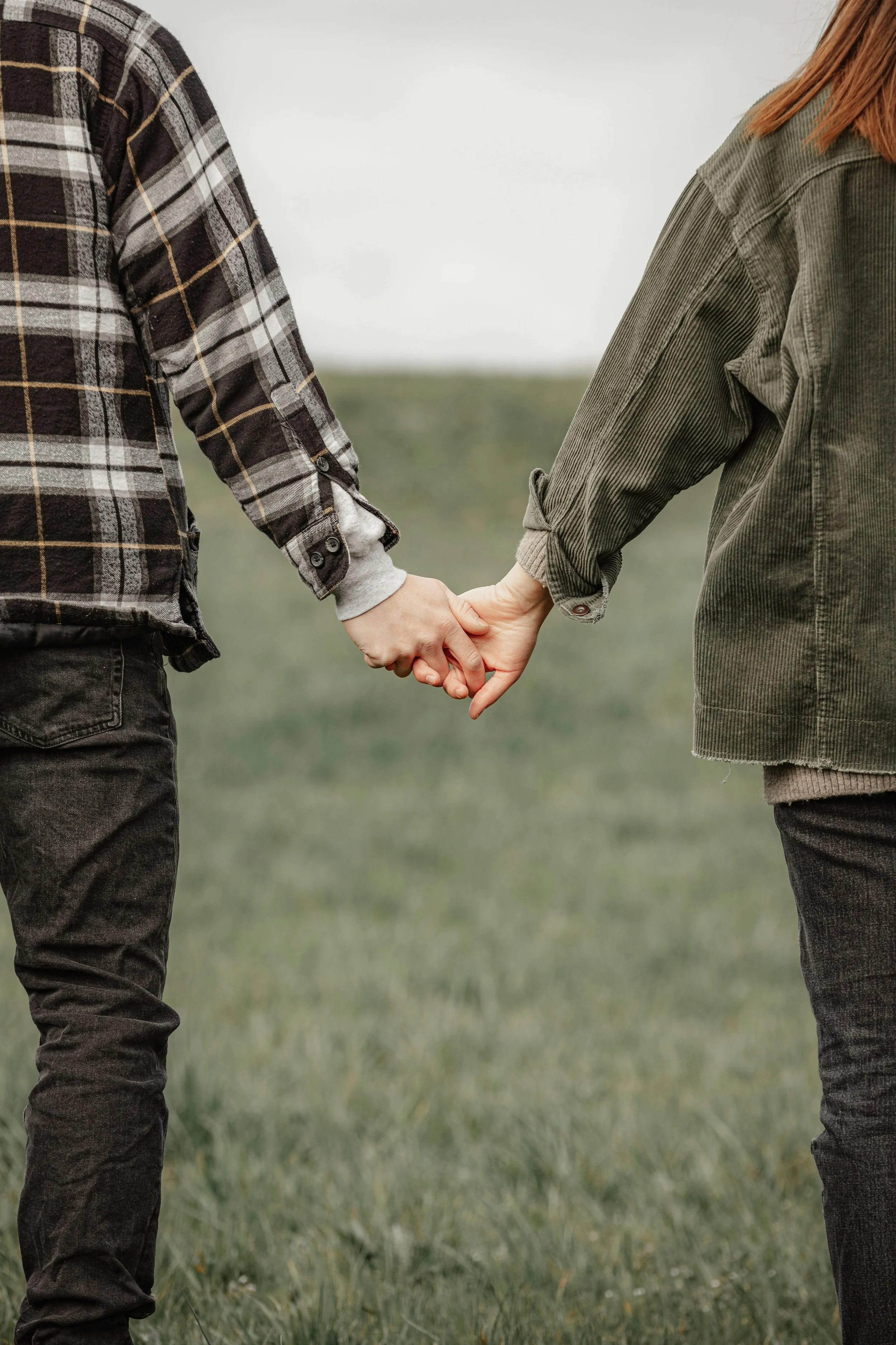 A man and a woman holding hands outdoors on a grassy field.