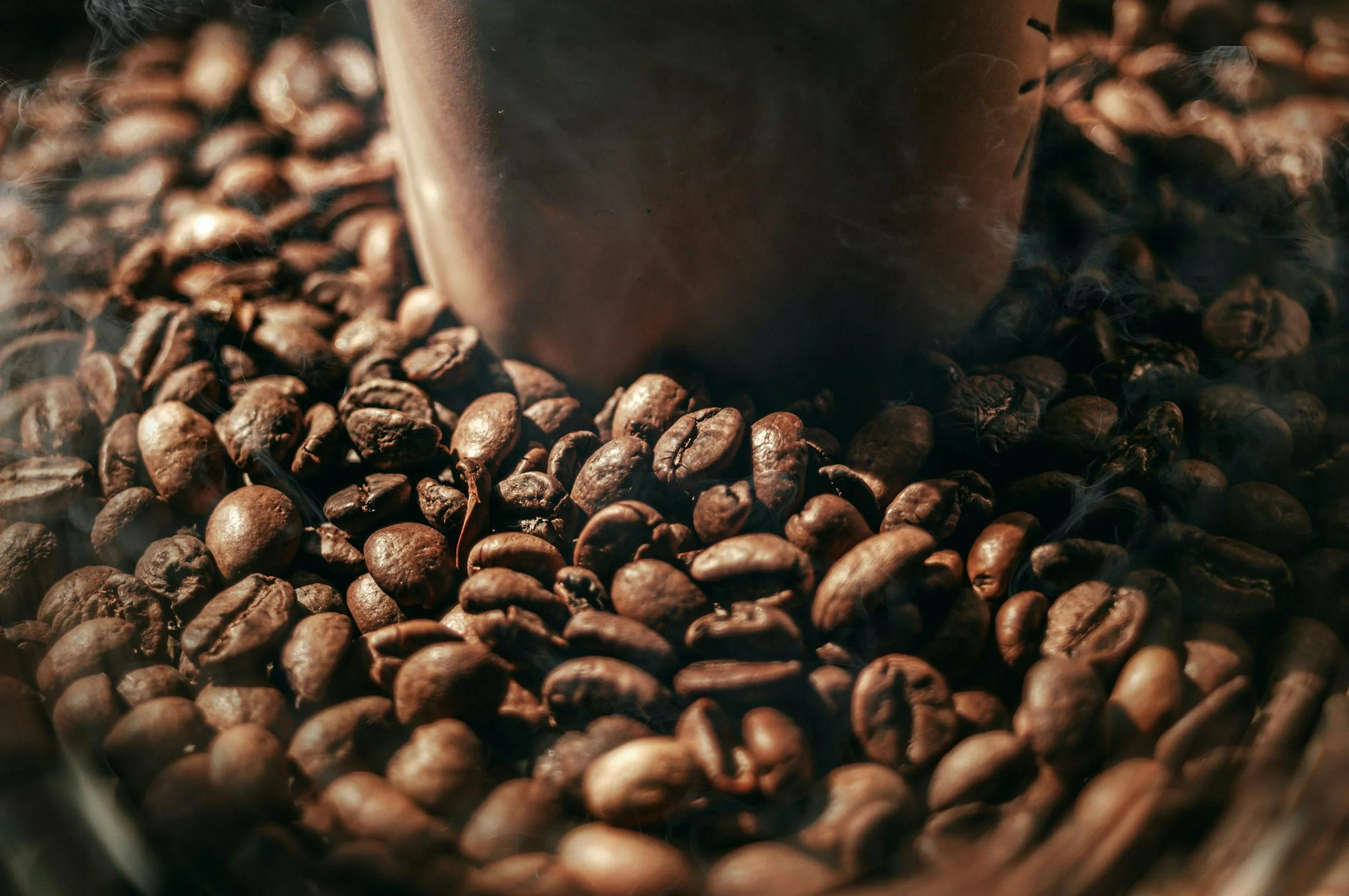 A close-up view of roasted coffee beans with a blurred coffee cup in the background.
