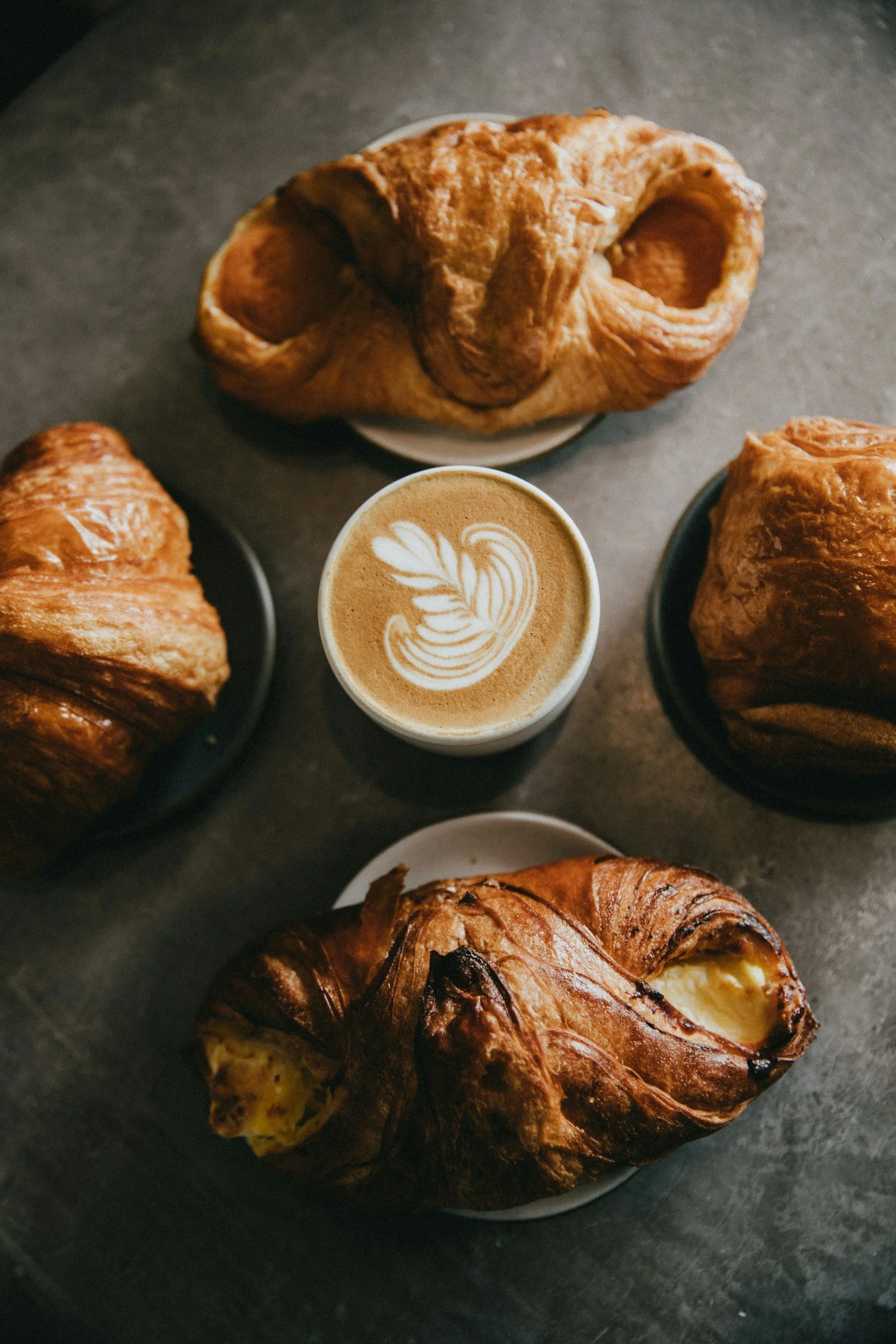 Assorted pastries and a latte with latte art on a dark table.