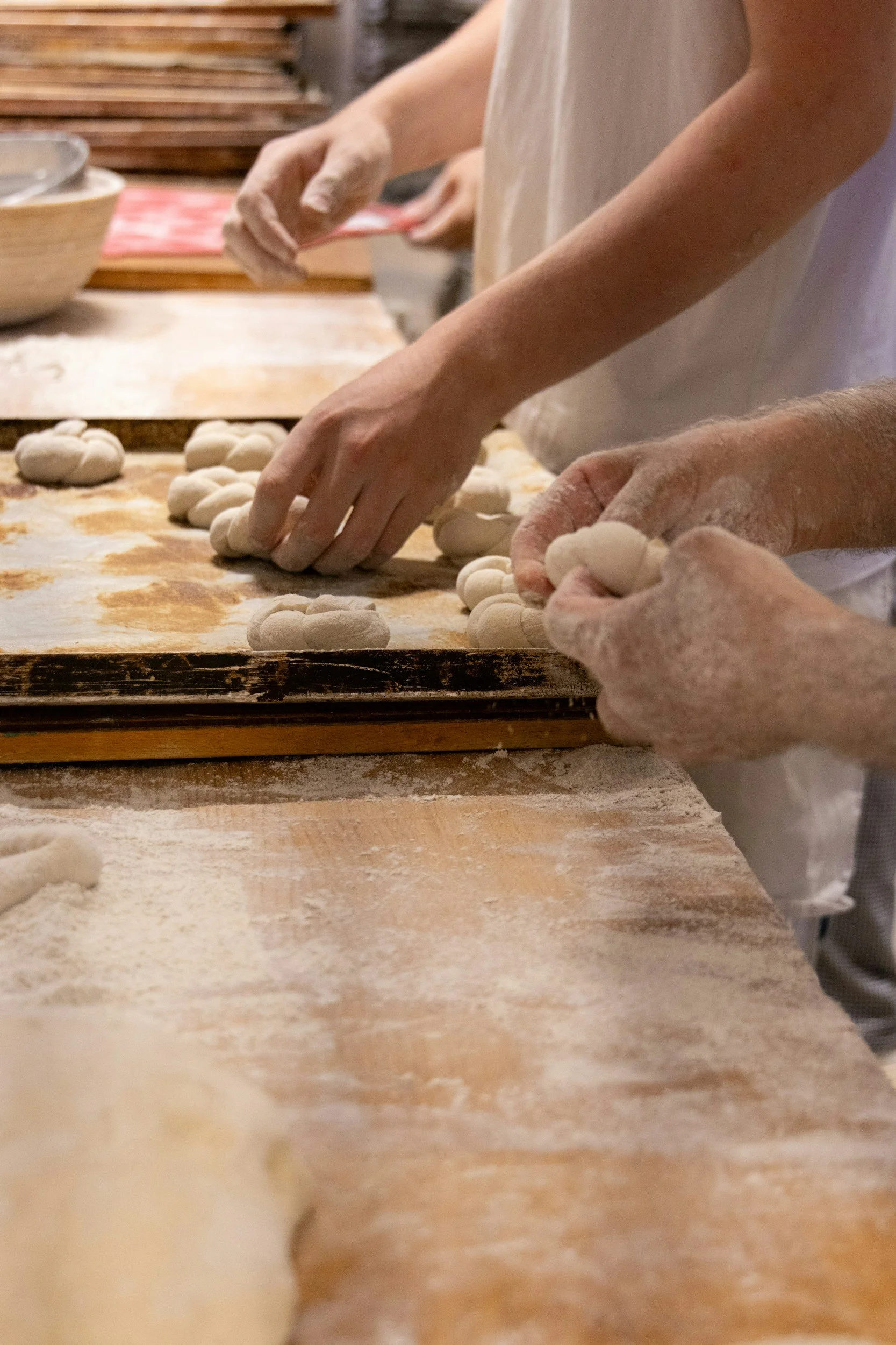 People making dough balls on a floured wooden surface in a bakery kitchen.