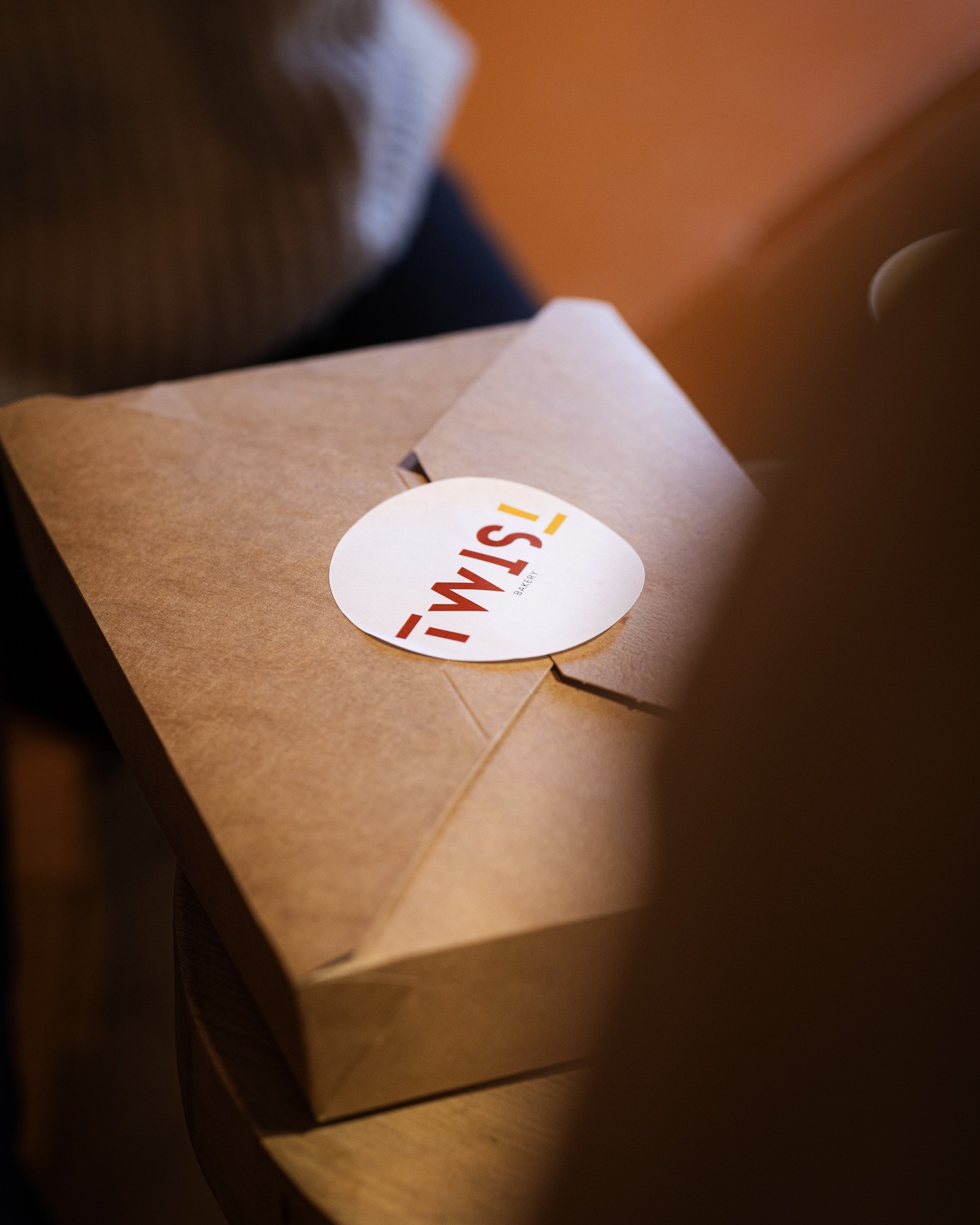 A cardboard Takeout box from TWIST Bakery and Coffee Shop on a wooden surface.