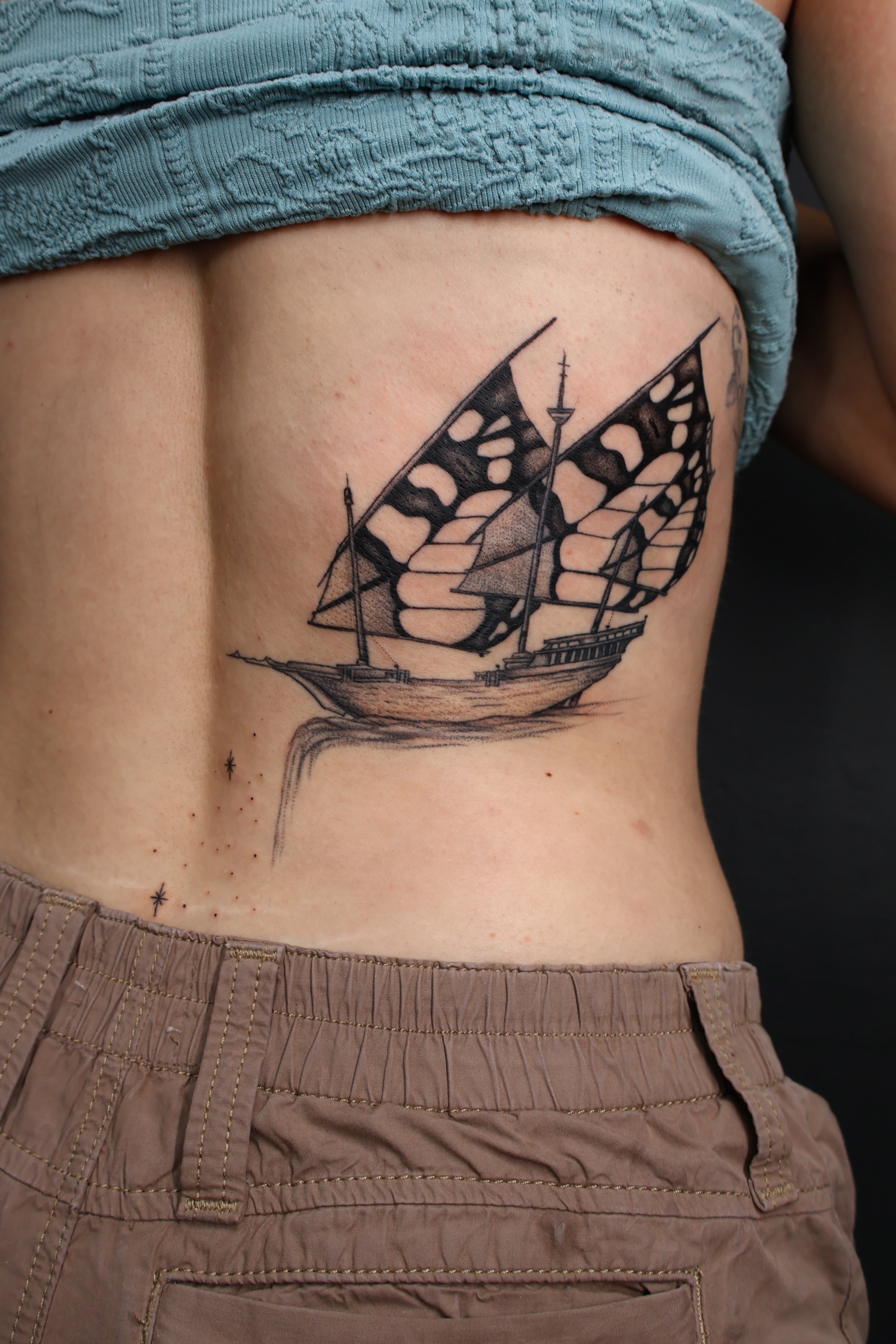 Tattoo of a ship with butterfly wings replacing the sails on the person's side ribcage.
