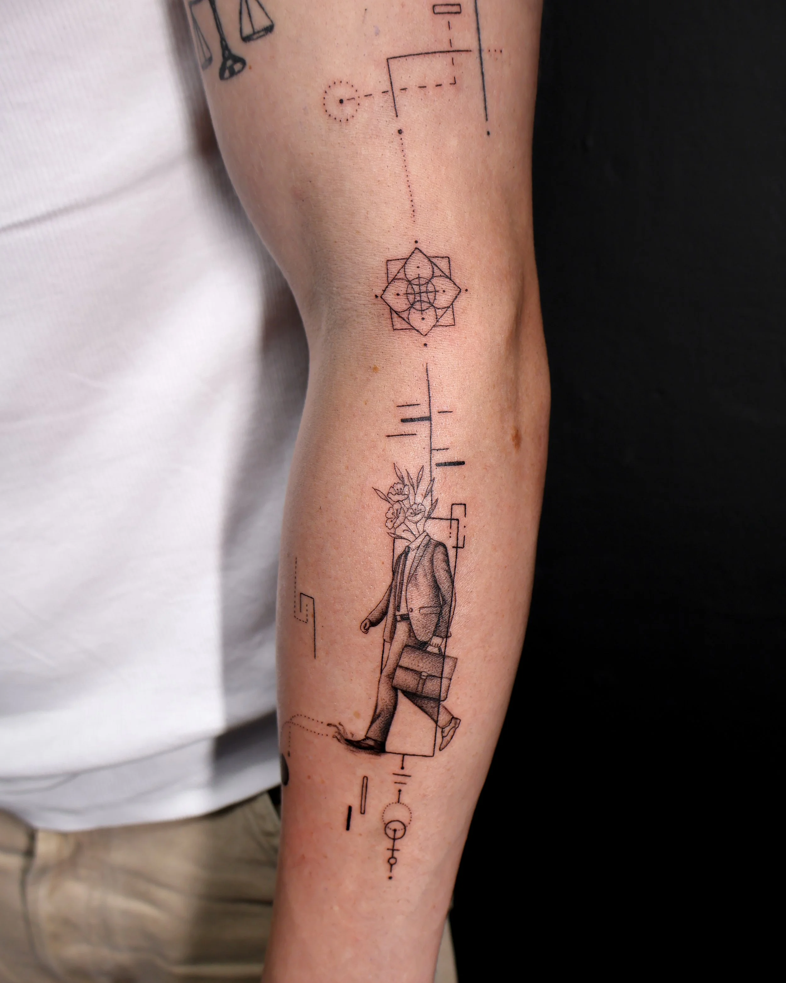 Tattoo of a person with a flower head carrying a briefcase, surrounded by geometric lines and symbols.