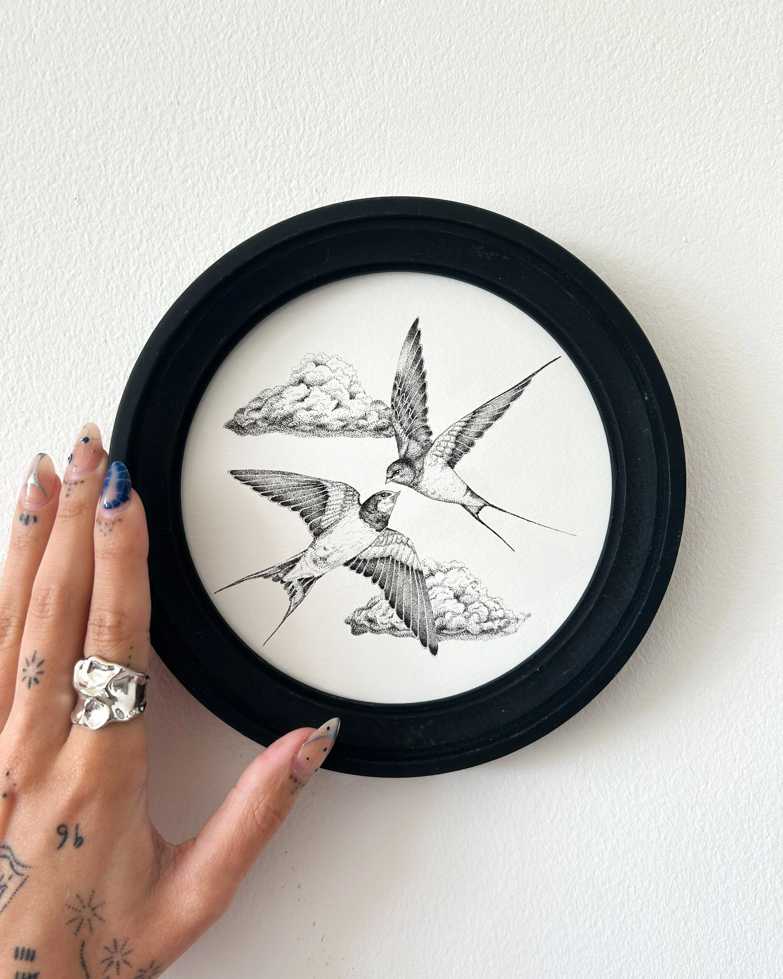 A black frame wall clock with a drawing of two flying swallows and clouds.