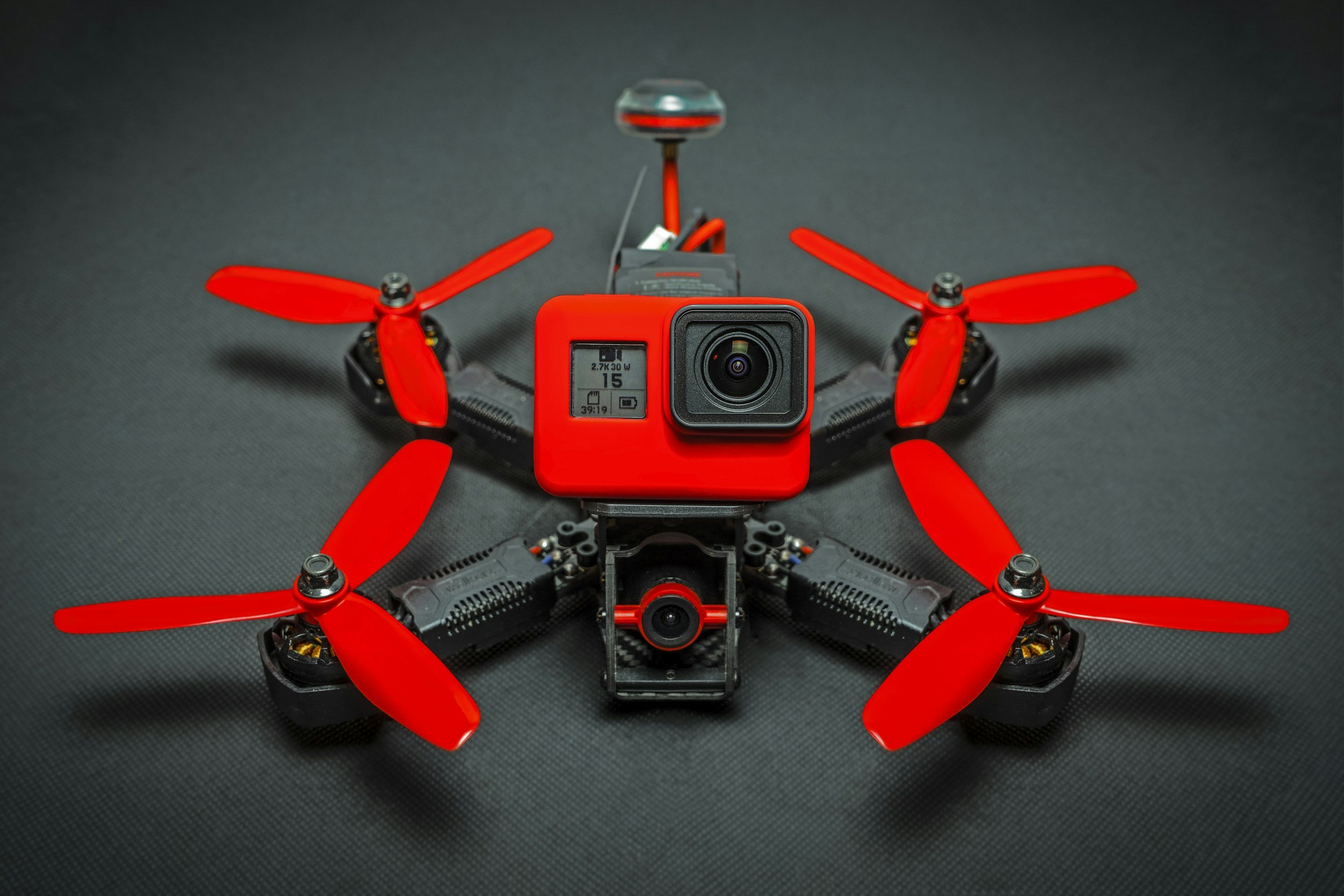 A racing drone with red propellers and a mounted action camera on top.
