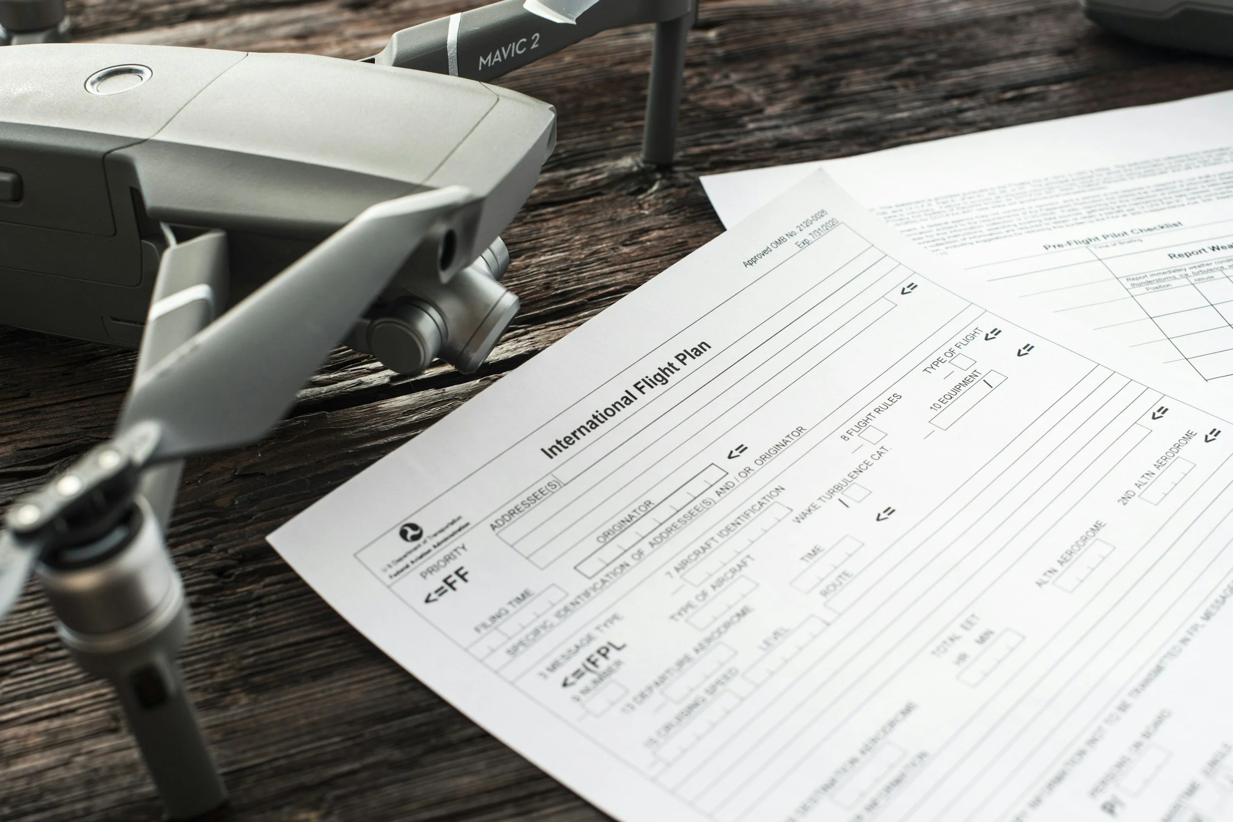 A drone sits on a wooden surface near a printed international flight plan document.