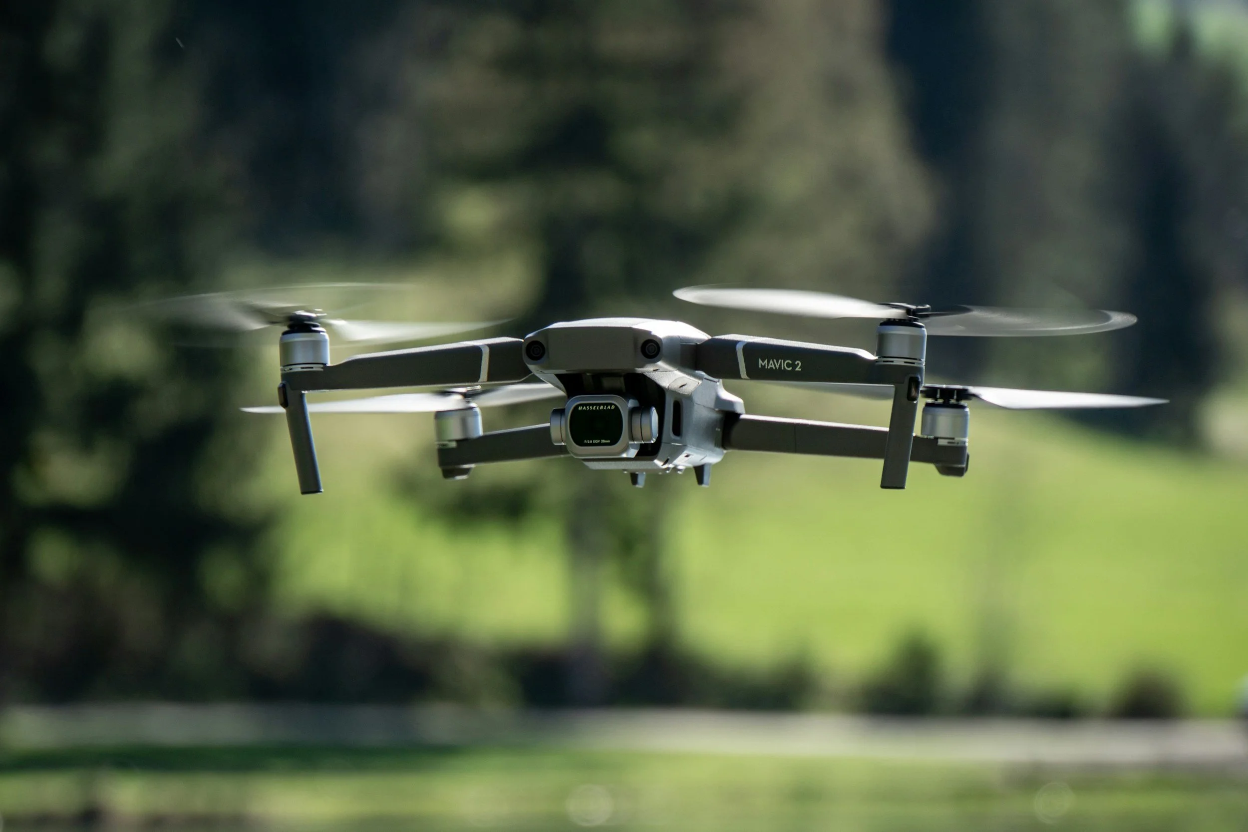 A drone flying outdoors in a park with green trees and grass in the background.