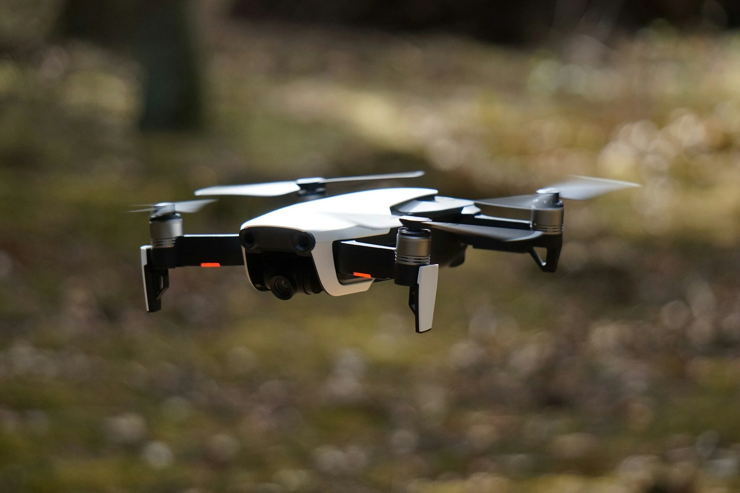 A white and black drone flying outdoors in a natural setting.