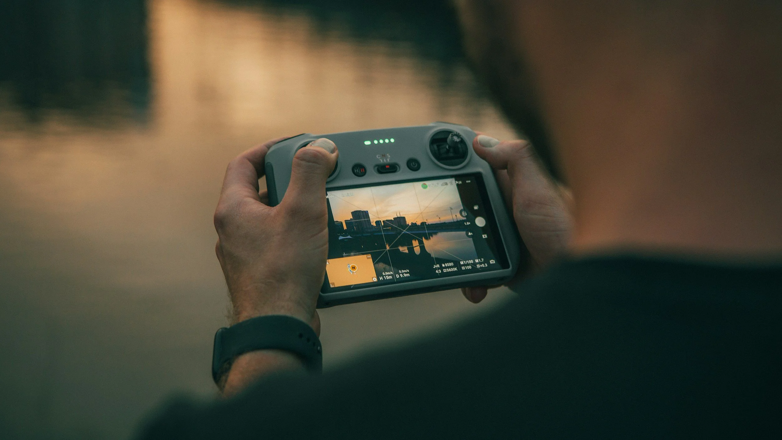 Person holding a camera, taking a photo of a sunset over a city skyline reflected in a body of water.