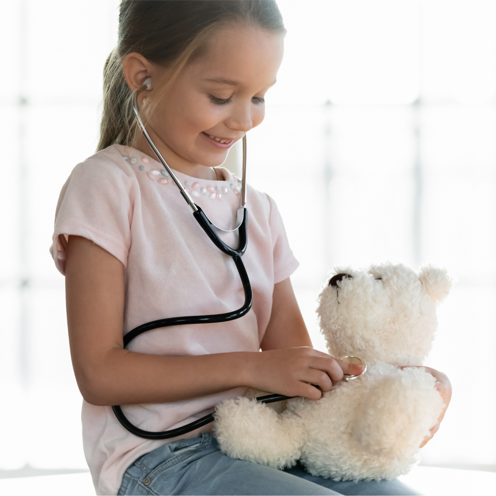 A young girl using a stethoscope on a stuffed teddy bear.