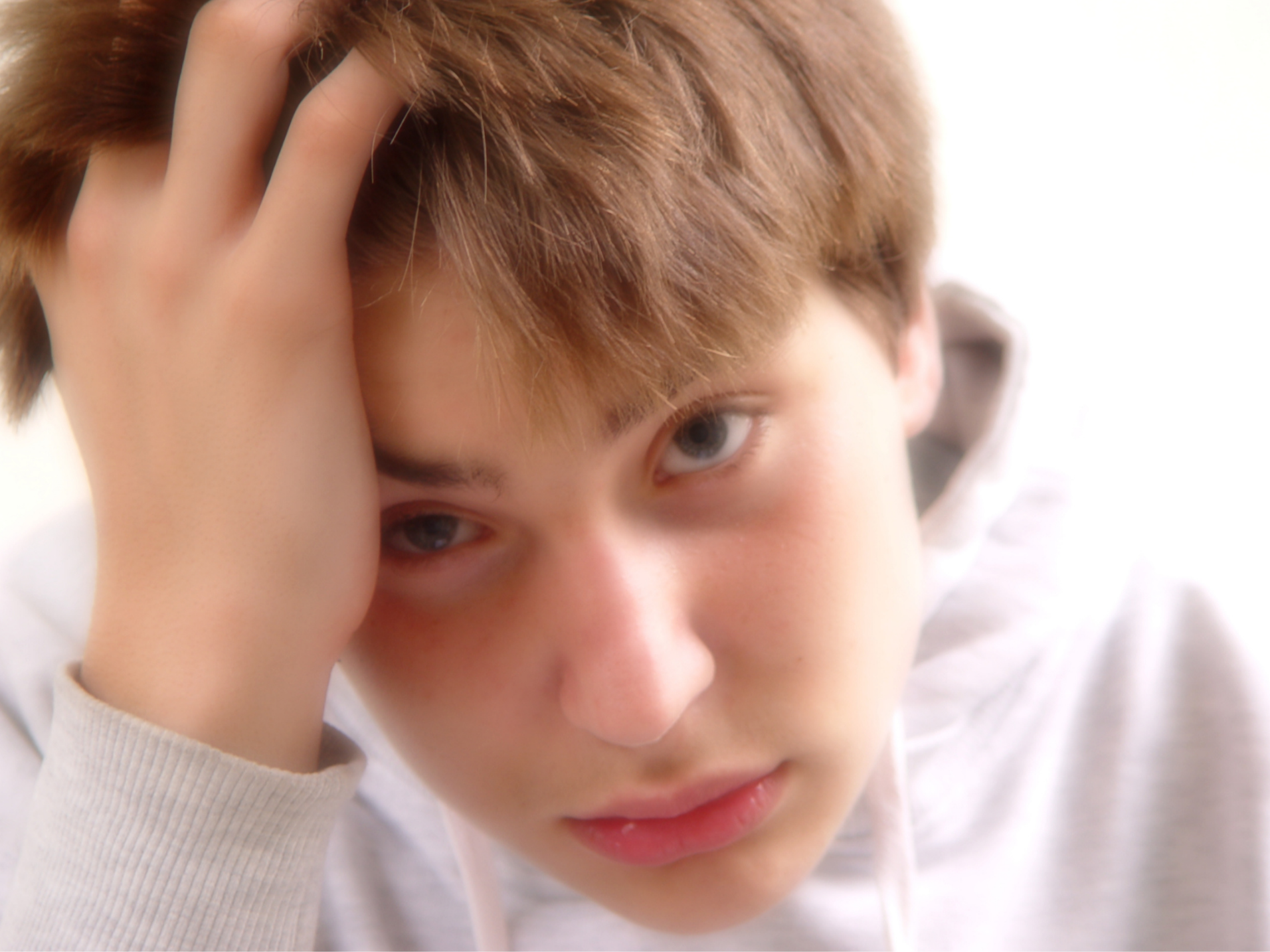 Close-up of a young person with red hair, gray eyes, and a worried or pensive expression, resting their head on their hand.