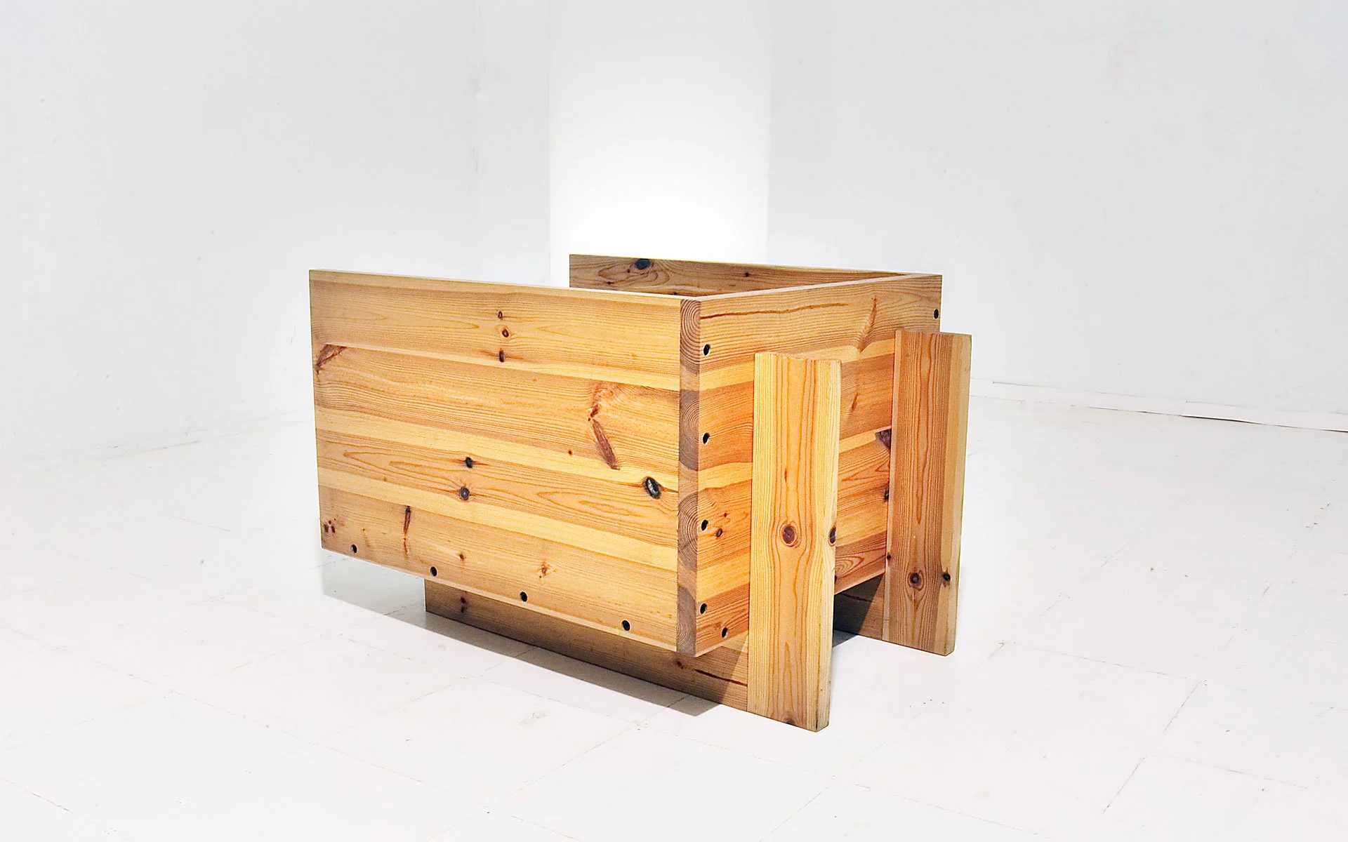 A wooden, rectangular-shaped, raised garden bed frame made of natural, light-colored wood in an empty white room.