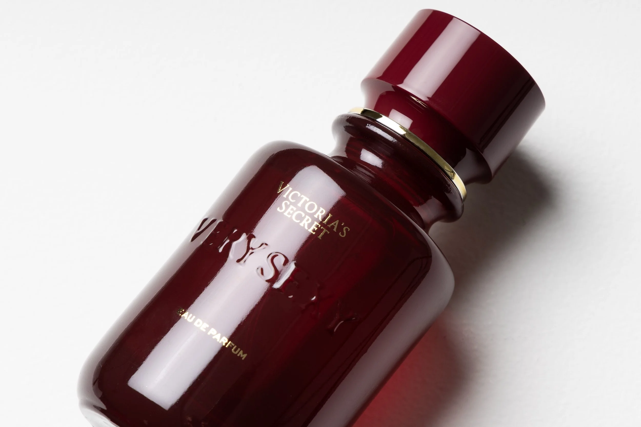 A dark red bottle of Victoria's Secret fragrance lying on a white surface.