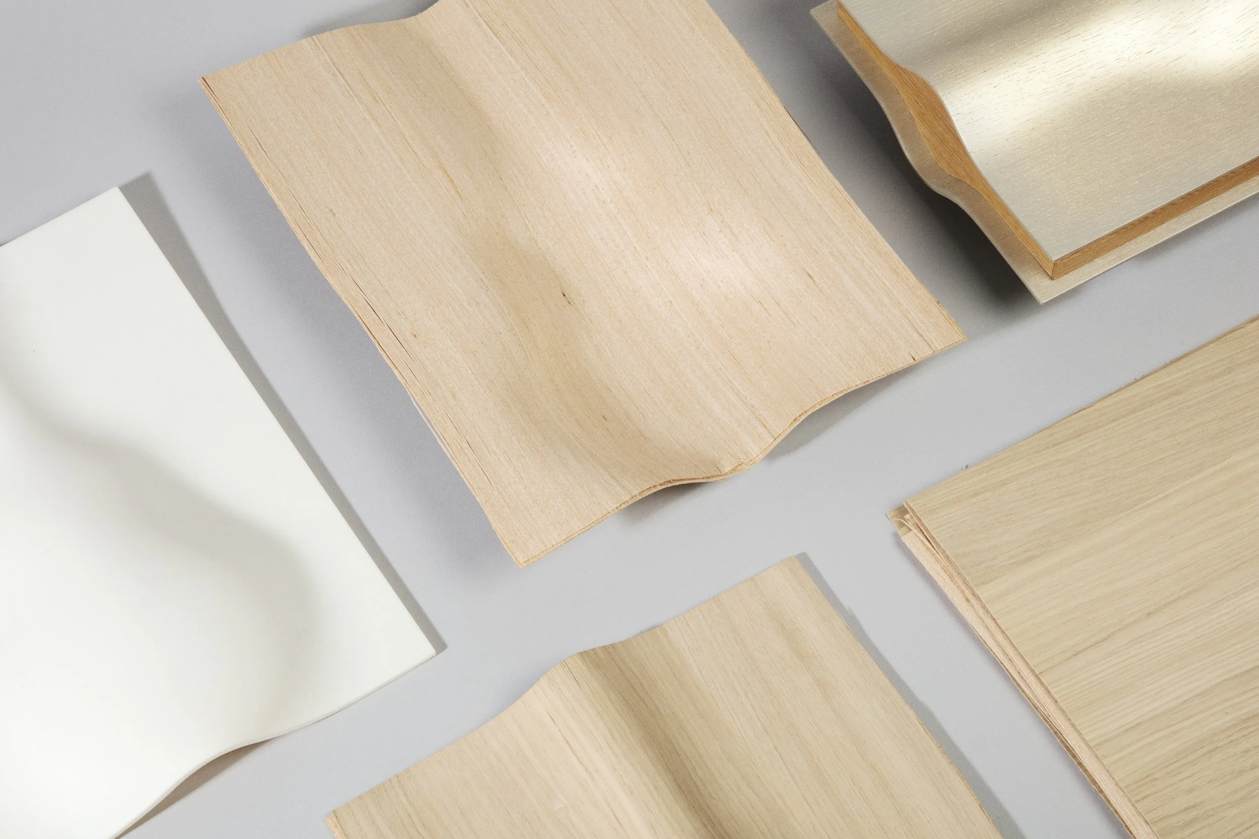 Various samples of wood veneer sheets in different shades and grain patterns laid out flat on a gray surface.