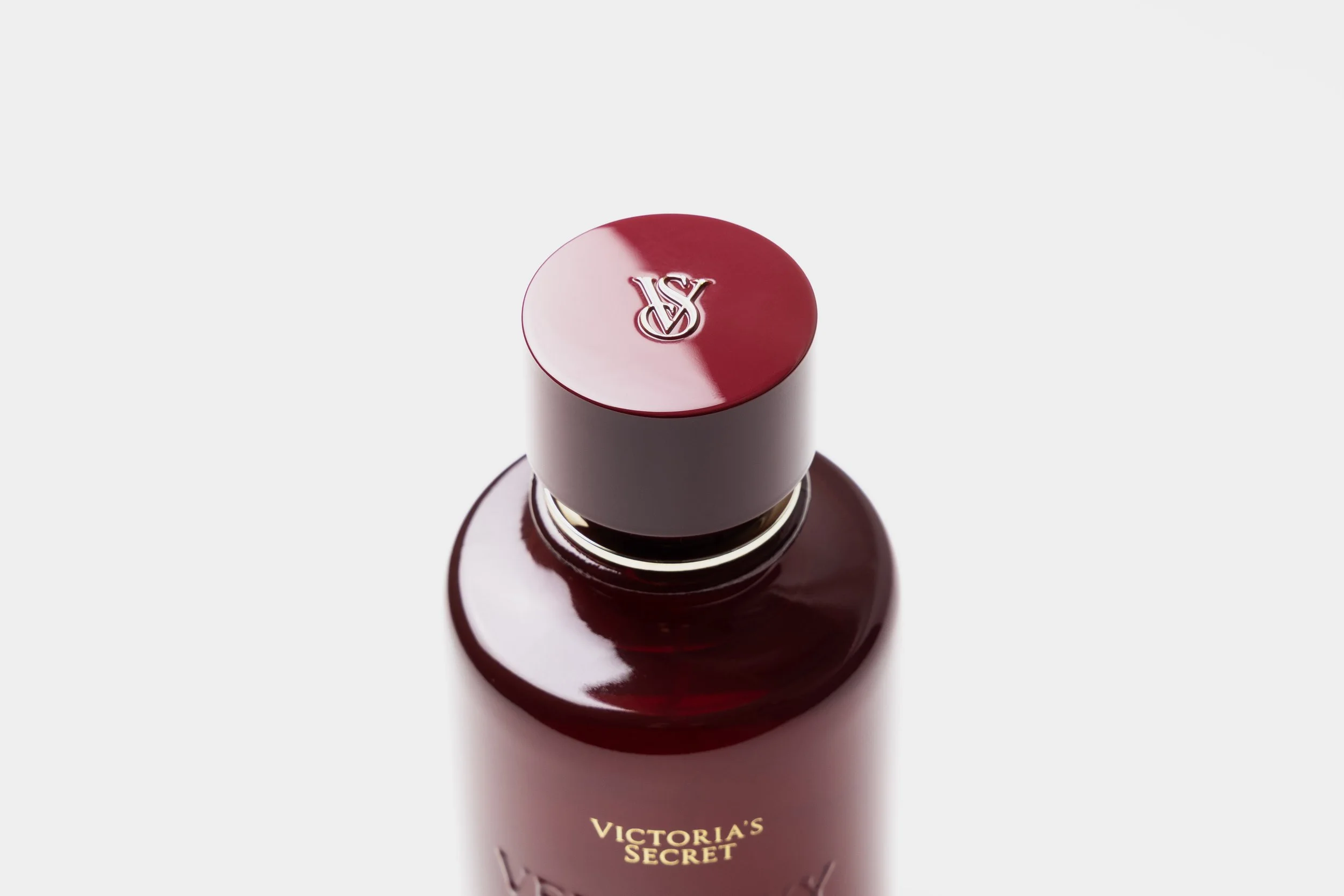 Close-up of a Victoria's Secret perfume bottle with a dark red cap that has Victoria's Secret logo, and part of the bottle's red body with gold lettering.