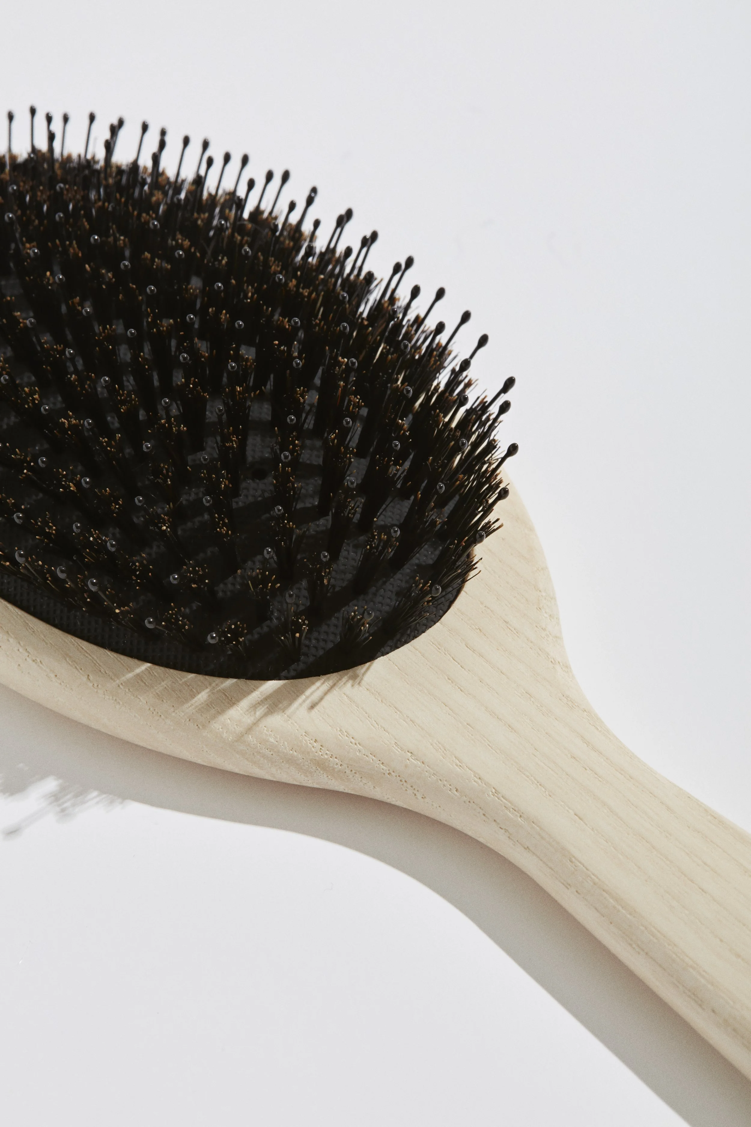 A close-up of a hairbrush with black bristles and a wooden handle.