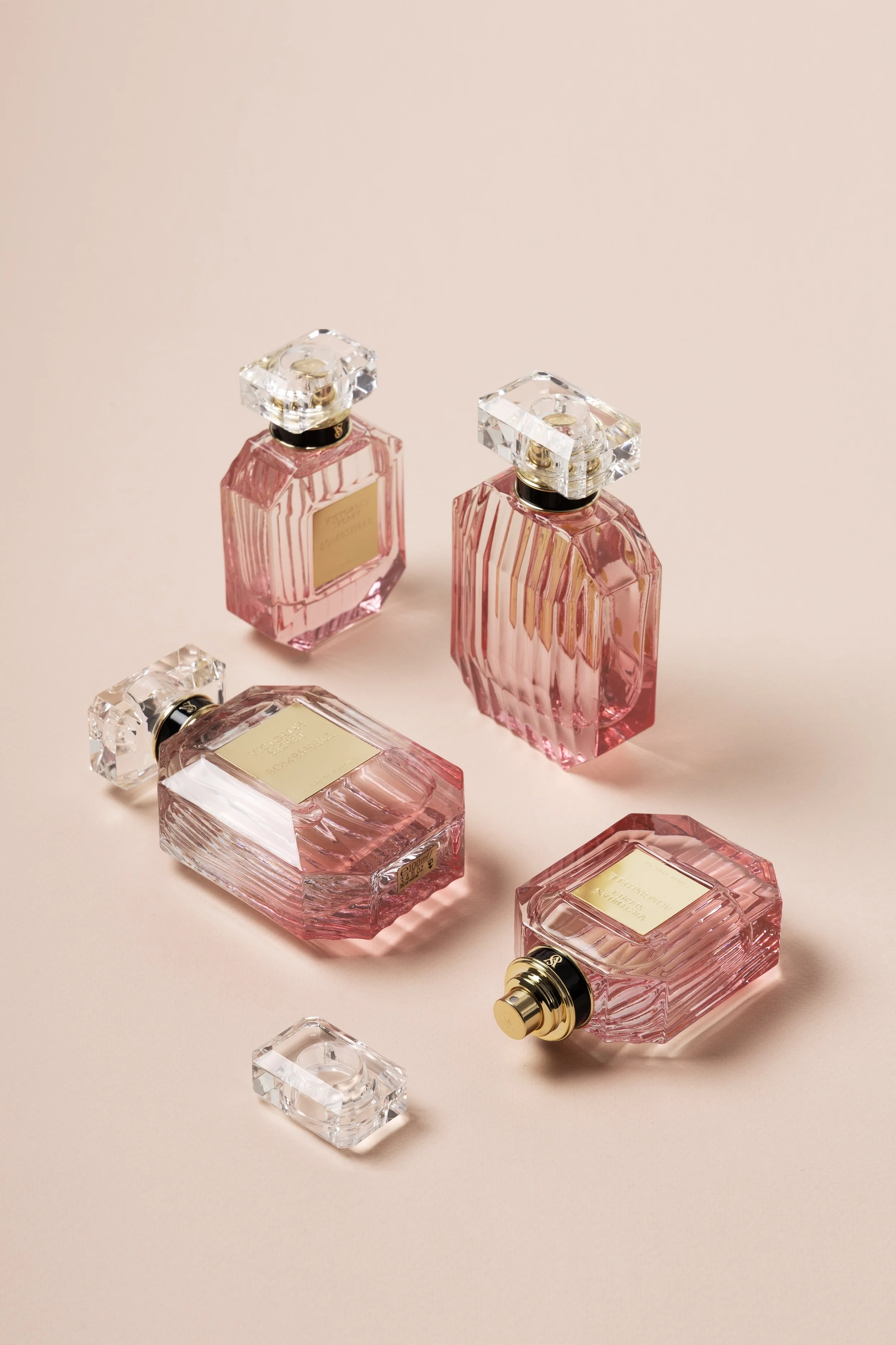 Four pink perfume bottles with gold labels and clear, square caps placed on a light pink surface.