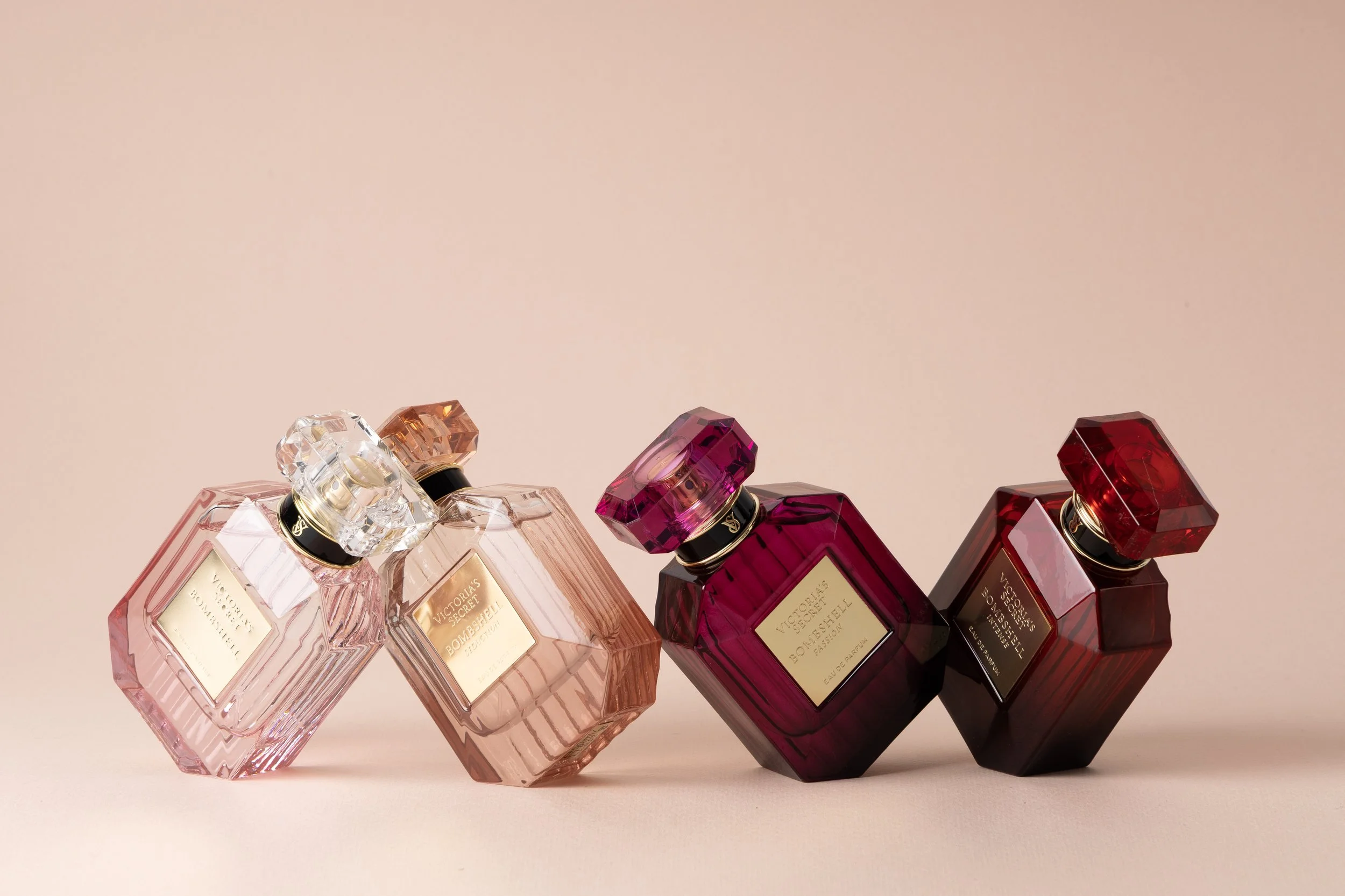 Four Victoria's Secret perfume bottles in pink, light pink, dark pink, and deep red, displayed against a light pink background.