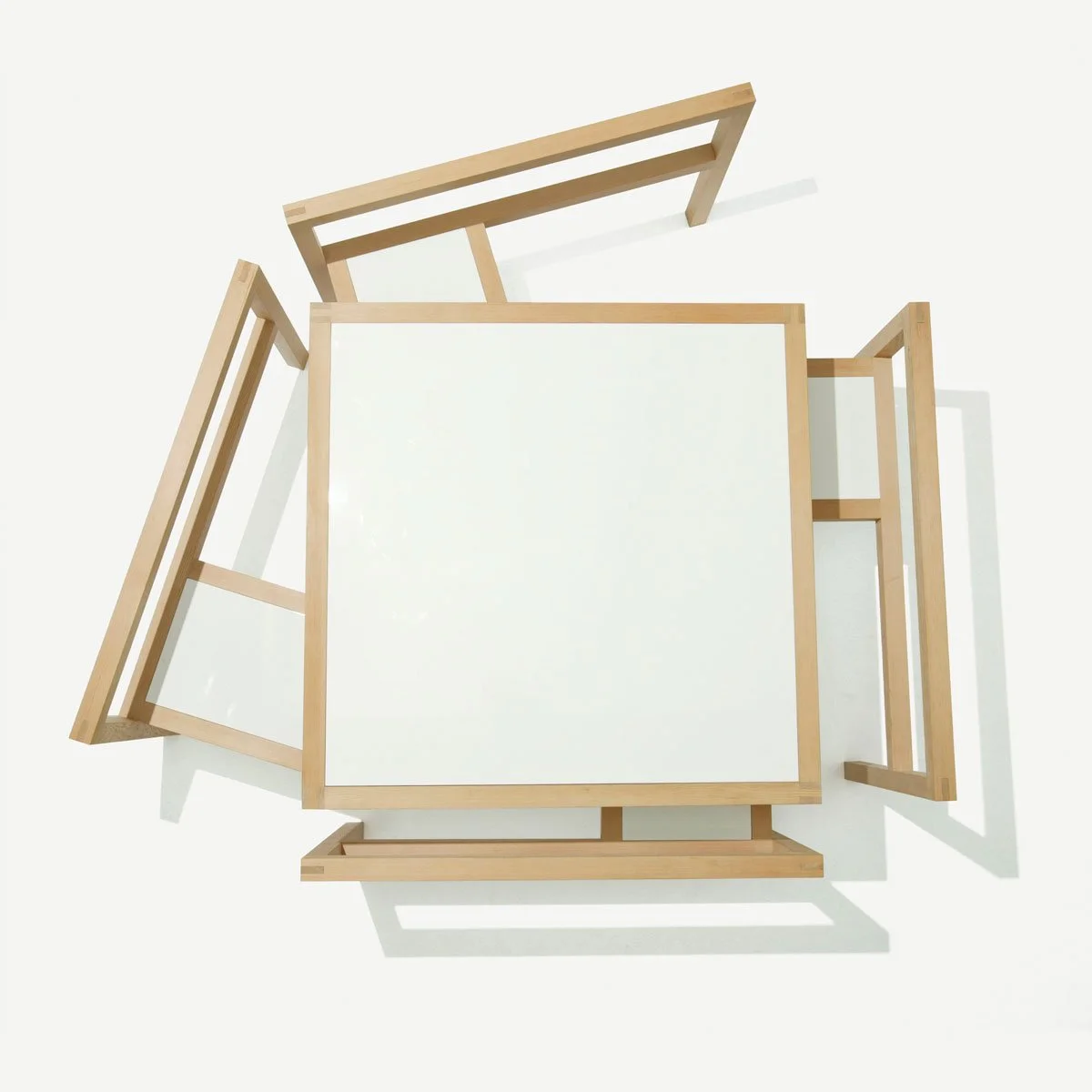 Top-down view of a white square table with a wooden frame, surrounded by four empty wooden picture frames on a white background.