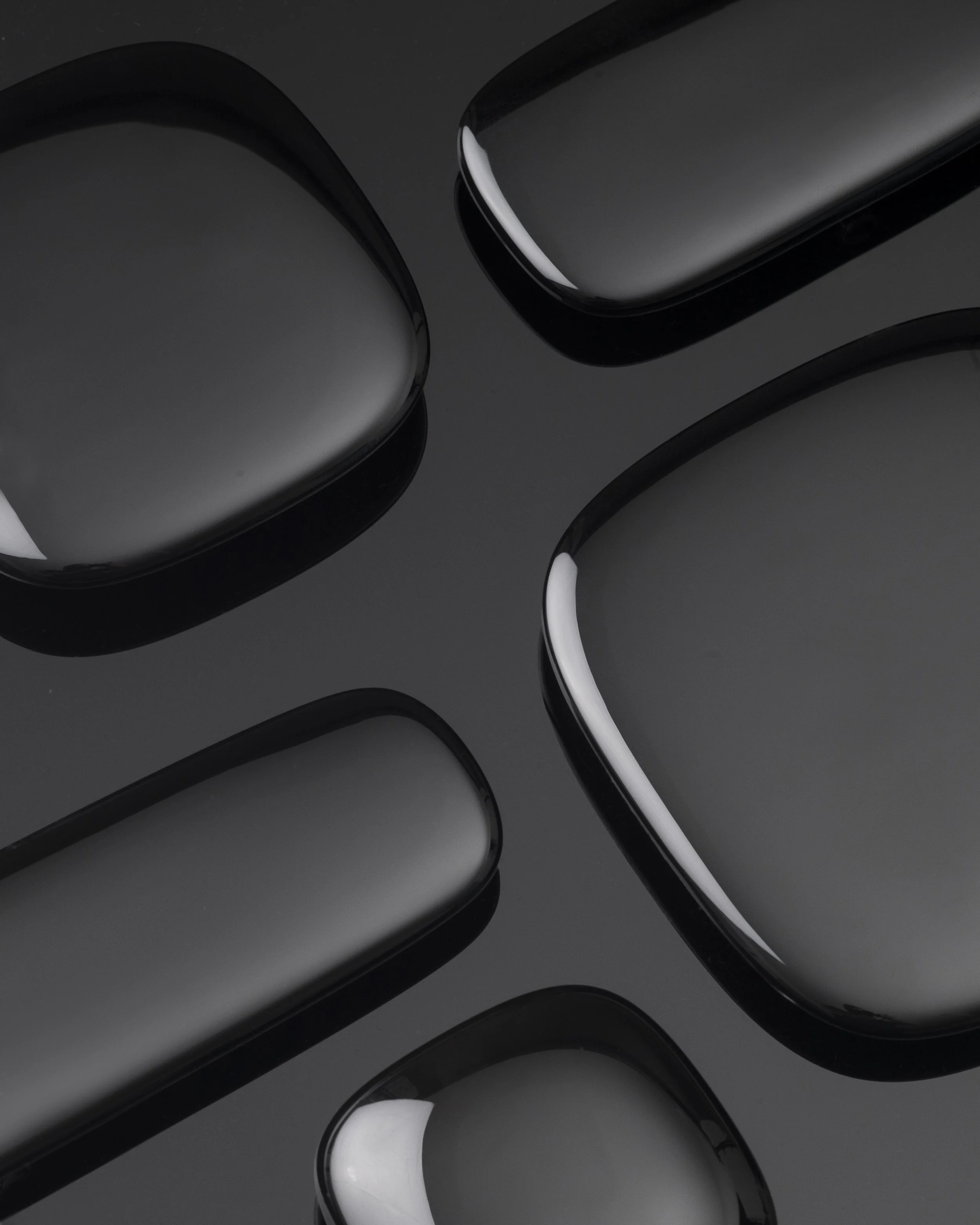 Close-up of several sleek, black, shiny, rounded rectangular objects with white reflections on a black surface.