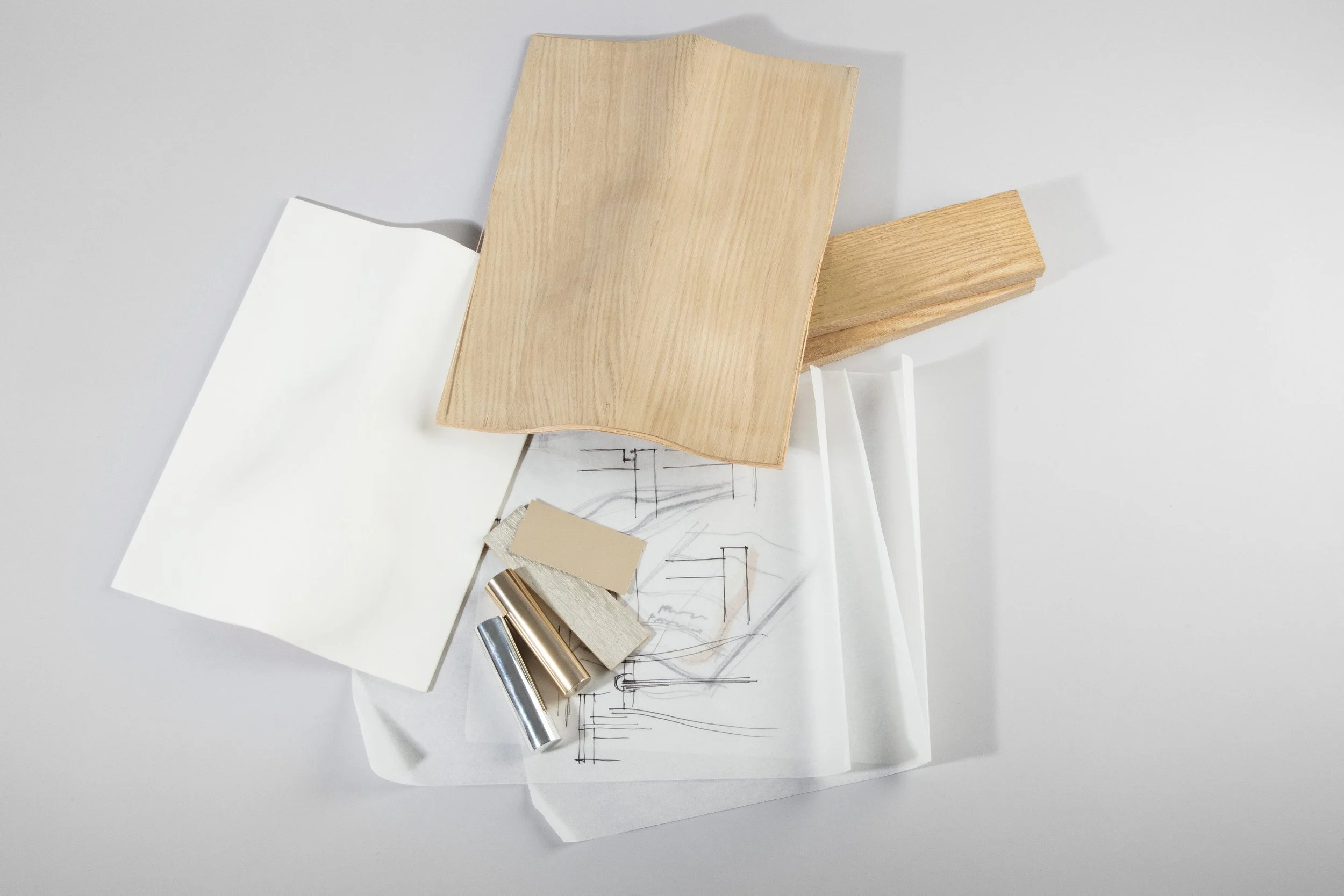 Arrangement of wooden, paper, and metal materials on a white surface, including sketches, small wood and metal samples, and two wooden planks.