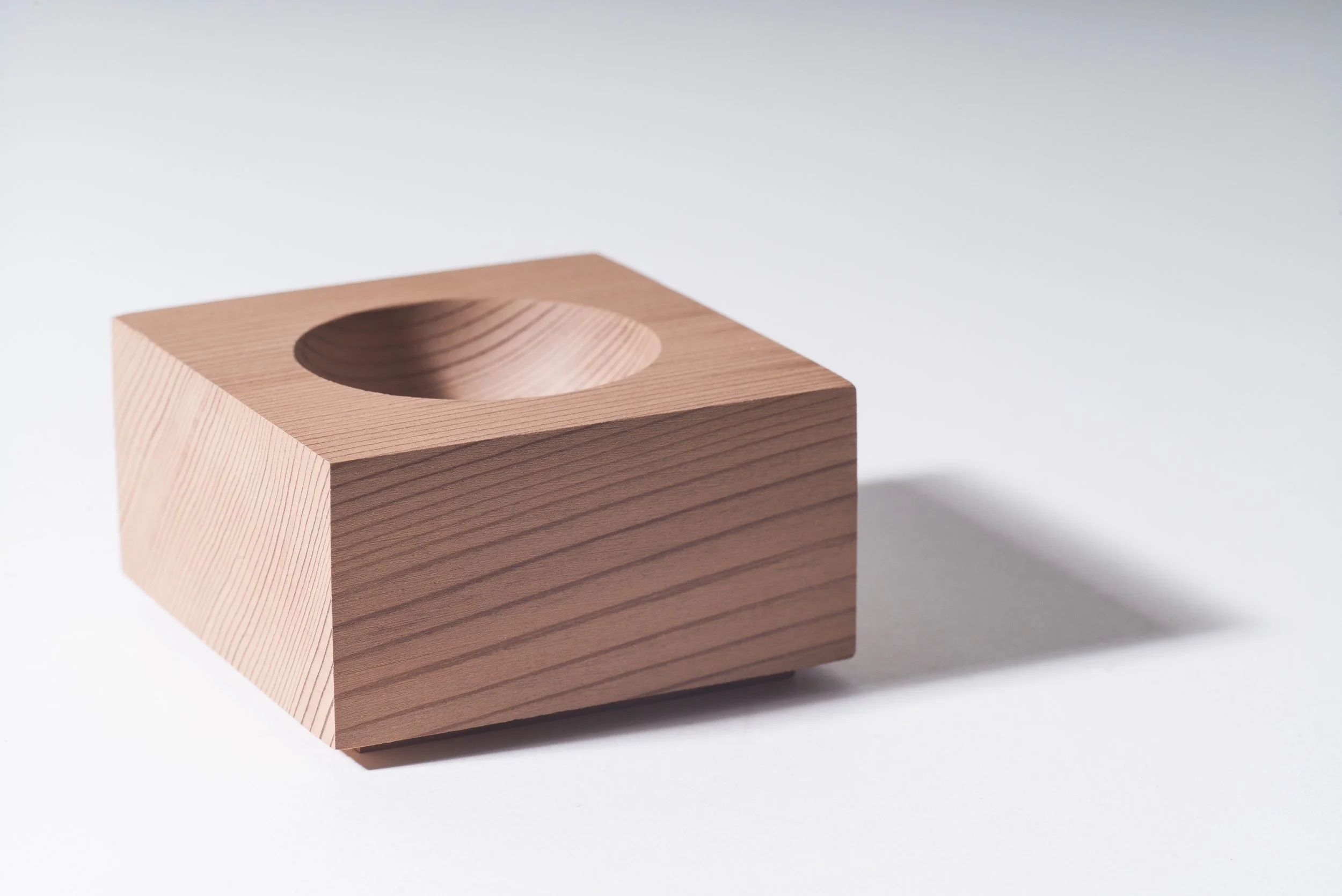 A wooden block with a circular hole in the center, placed on a white surface with a shadow to the right.