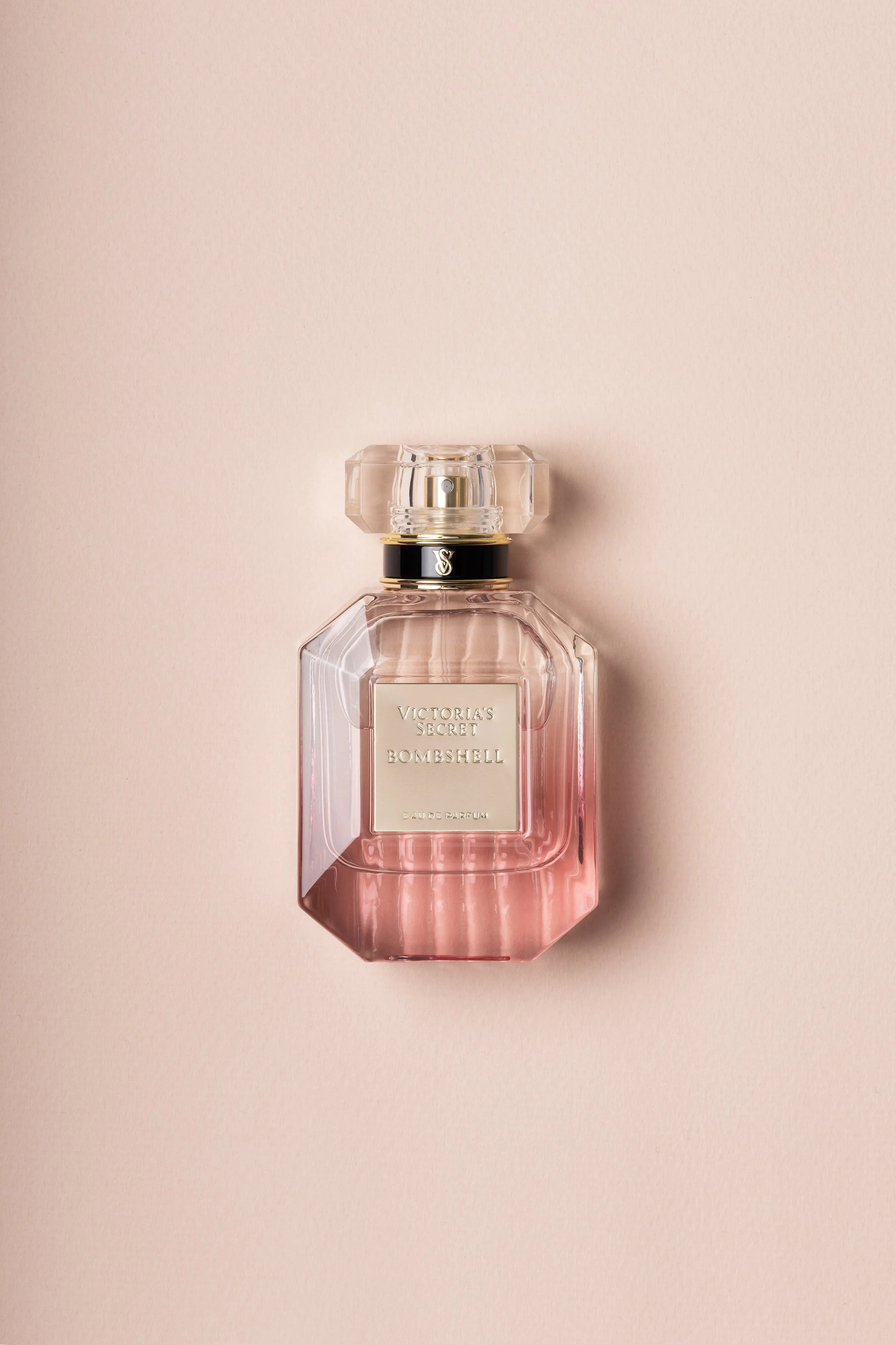 A pink Victoria's Secret Bombshell perfume bottle with a clear cap, placed on a light pink background.